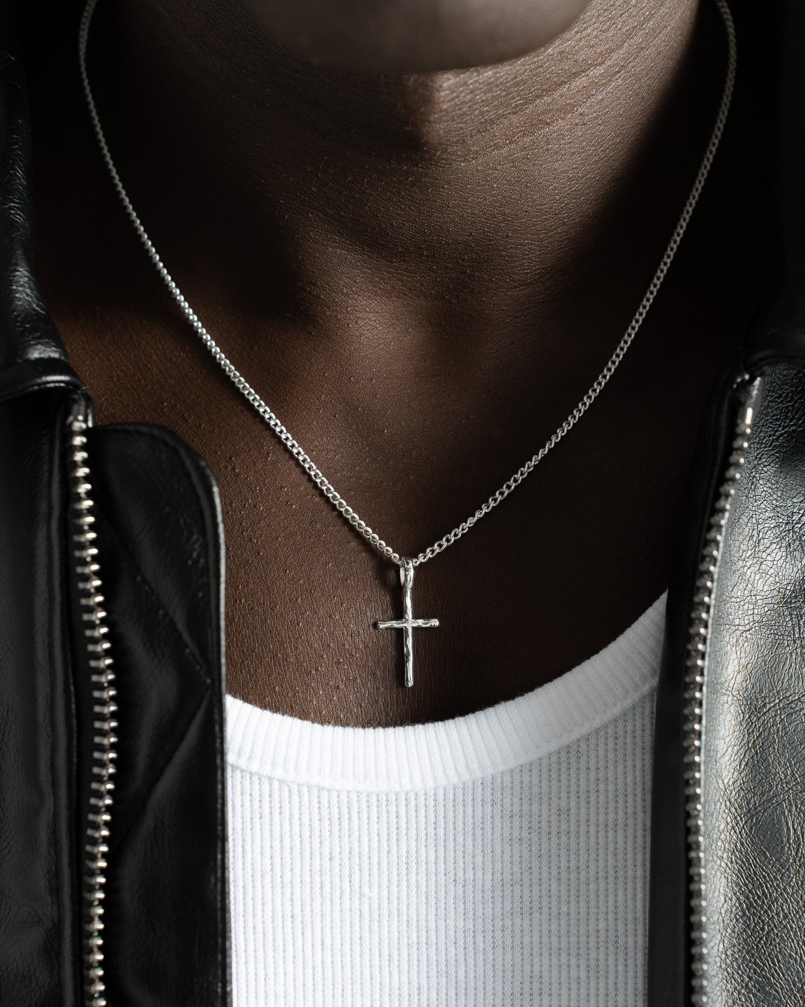 Silver cross necklace worn by a model in a leather jacket and white shirt
