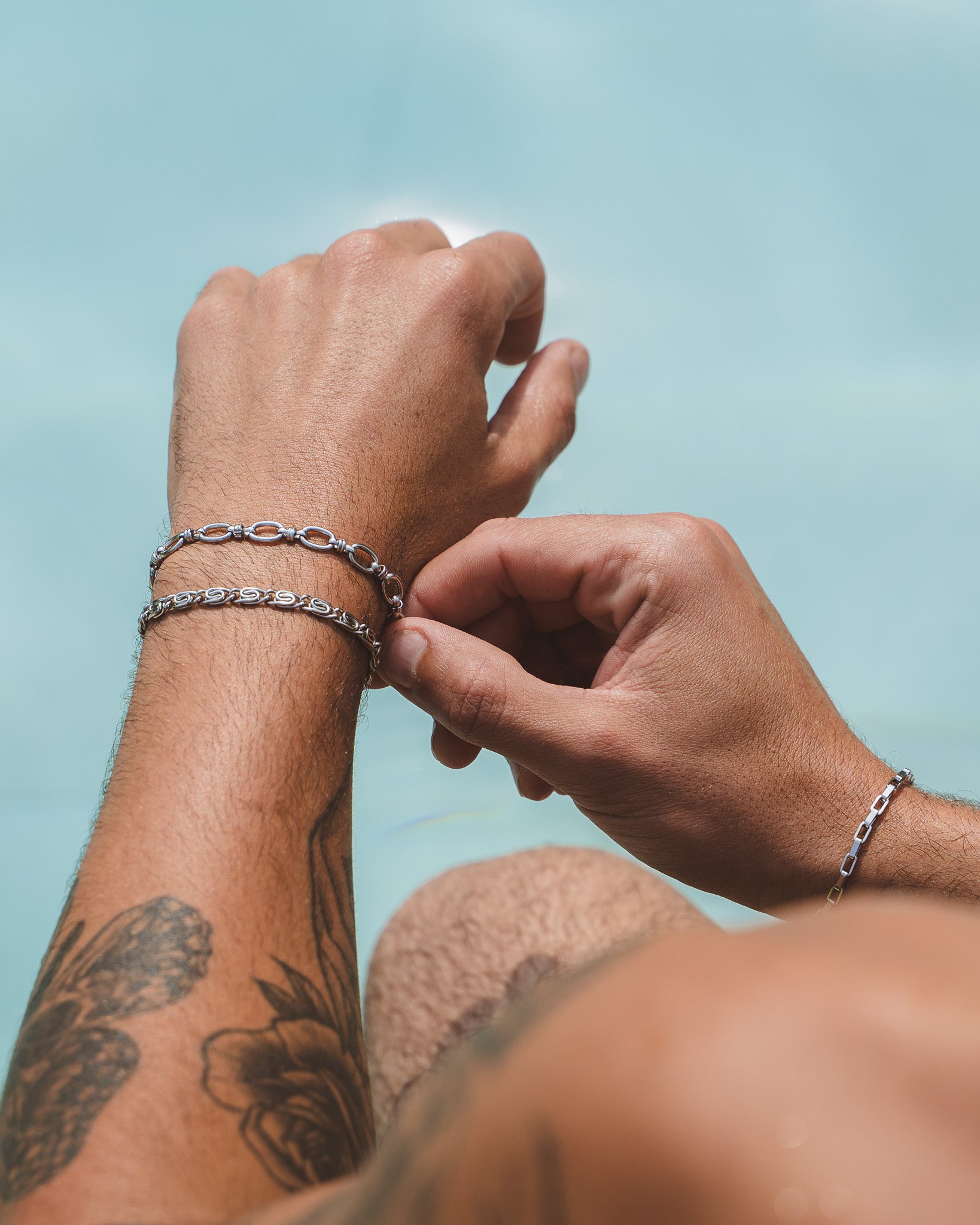Hand wearing BYBLOS silver bracelet stack against a blue water background