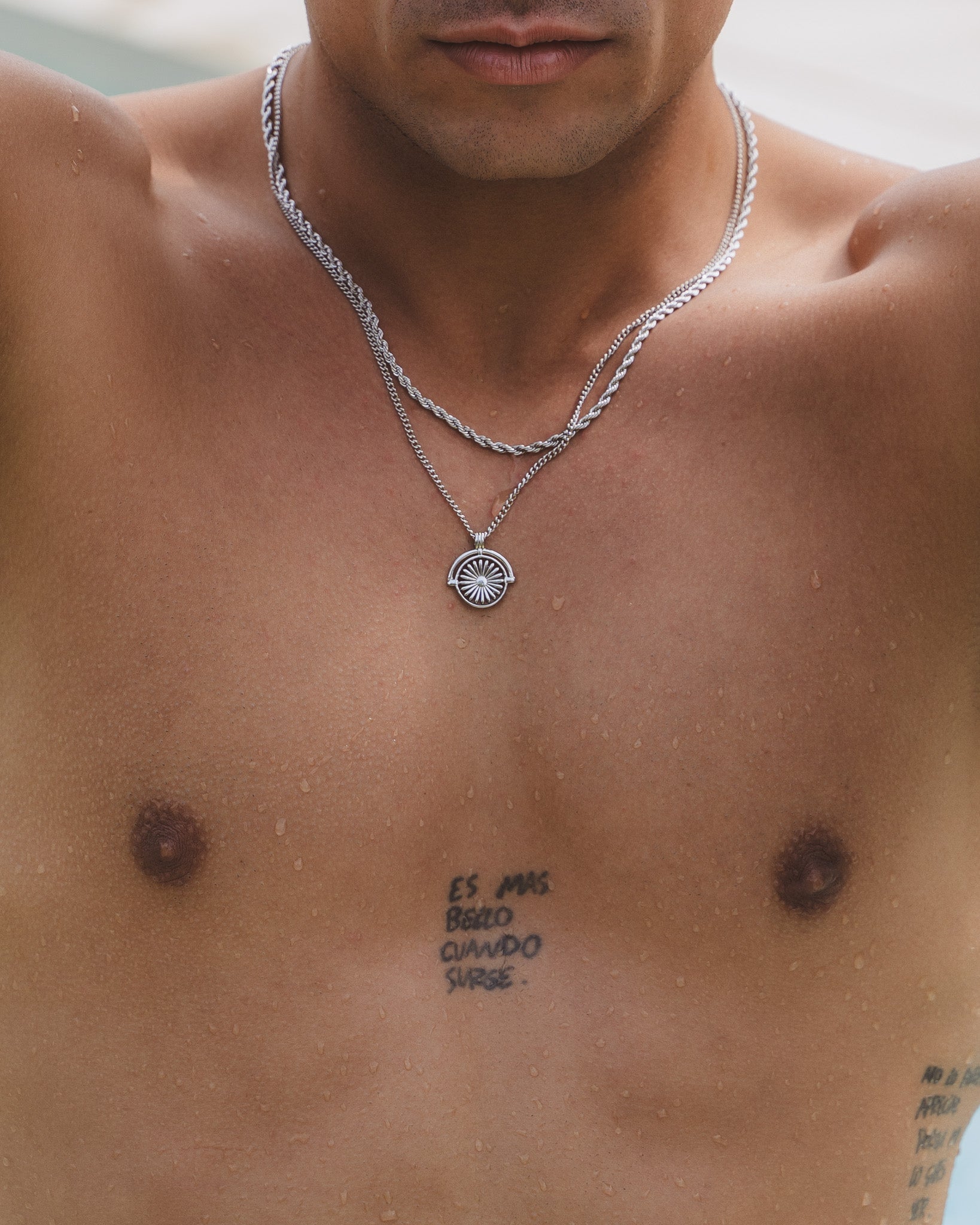 Close up of a man wearing layered Daisy silver necklaces with a pendant resting on his chest