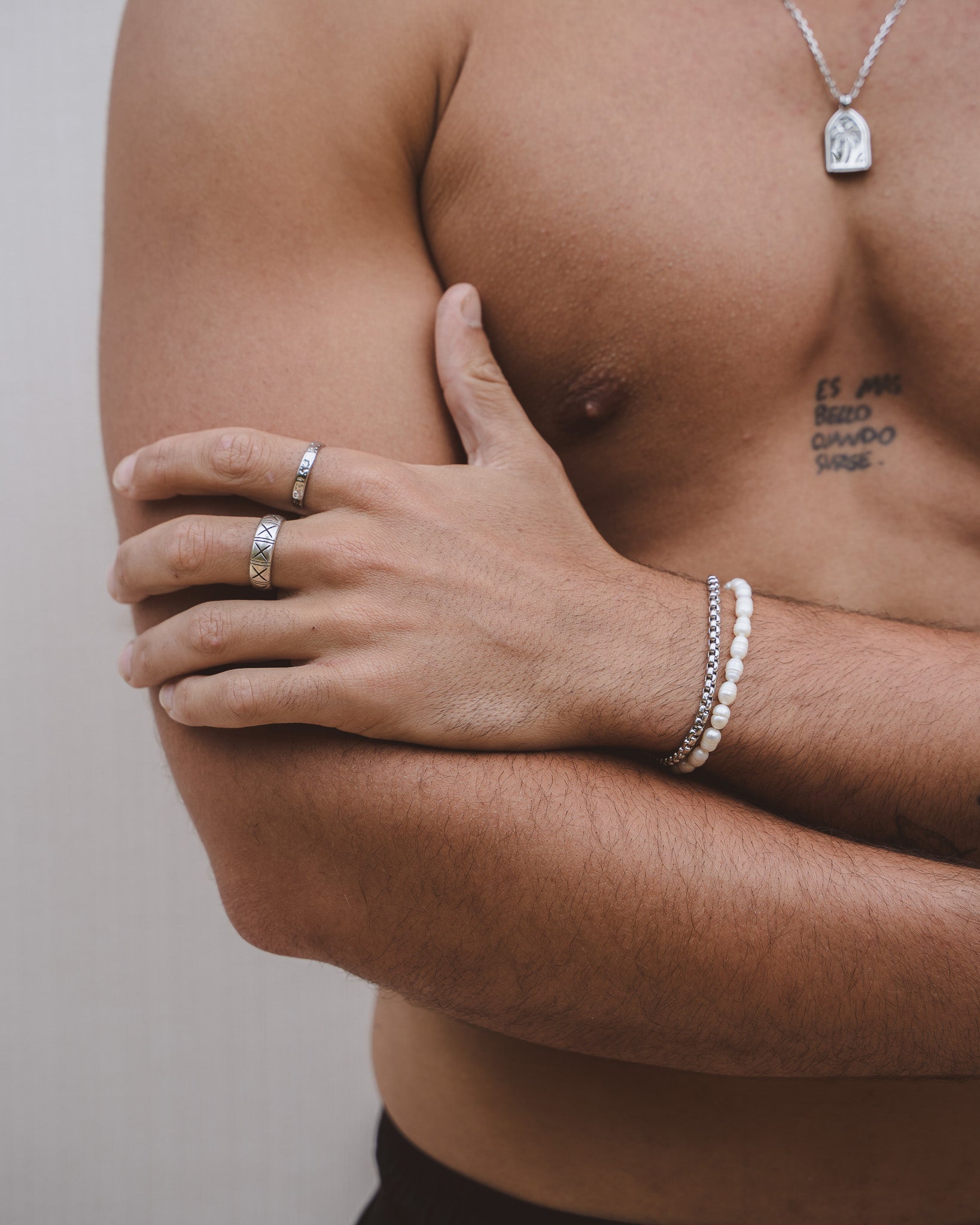 Silver ring with X motif worn on a finger; tattooed chest visible in background