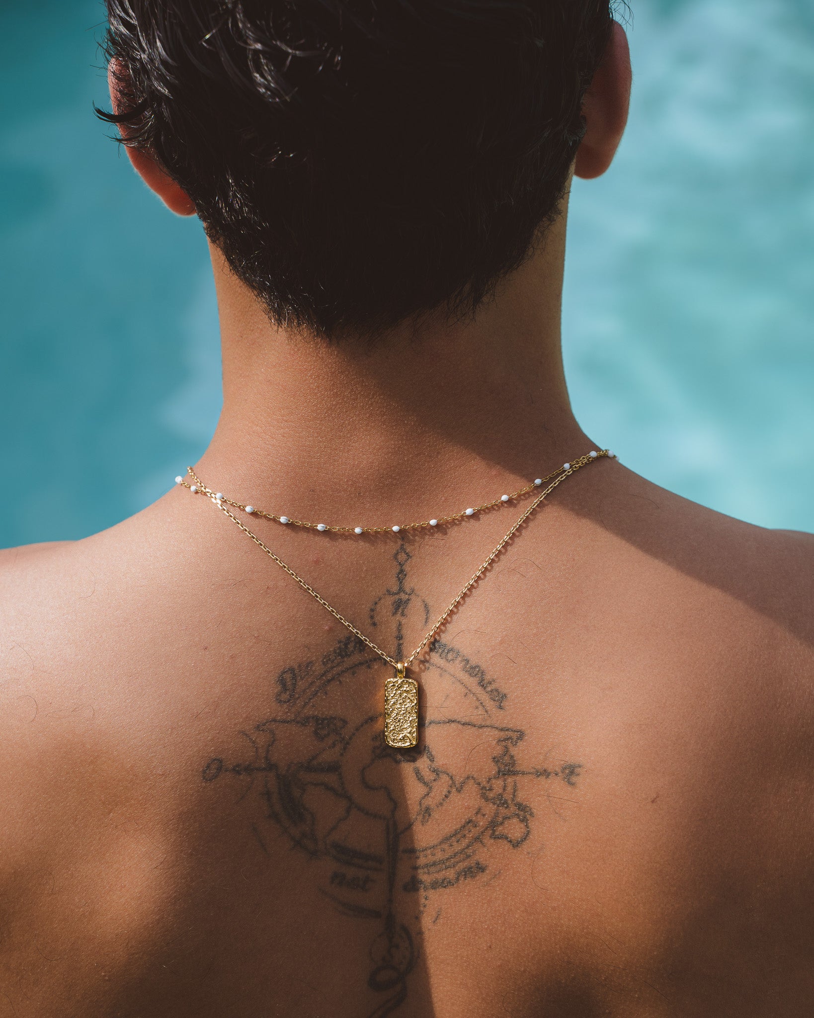 Front view of a man wearing two Moonrock gold necklaces with textured pendant and white bead accents