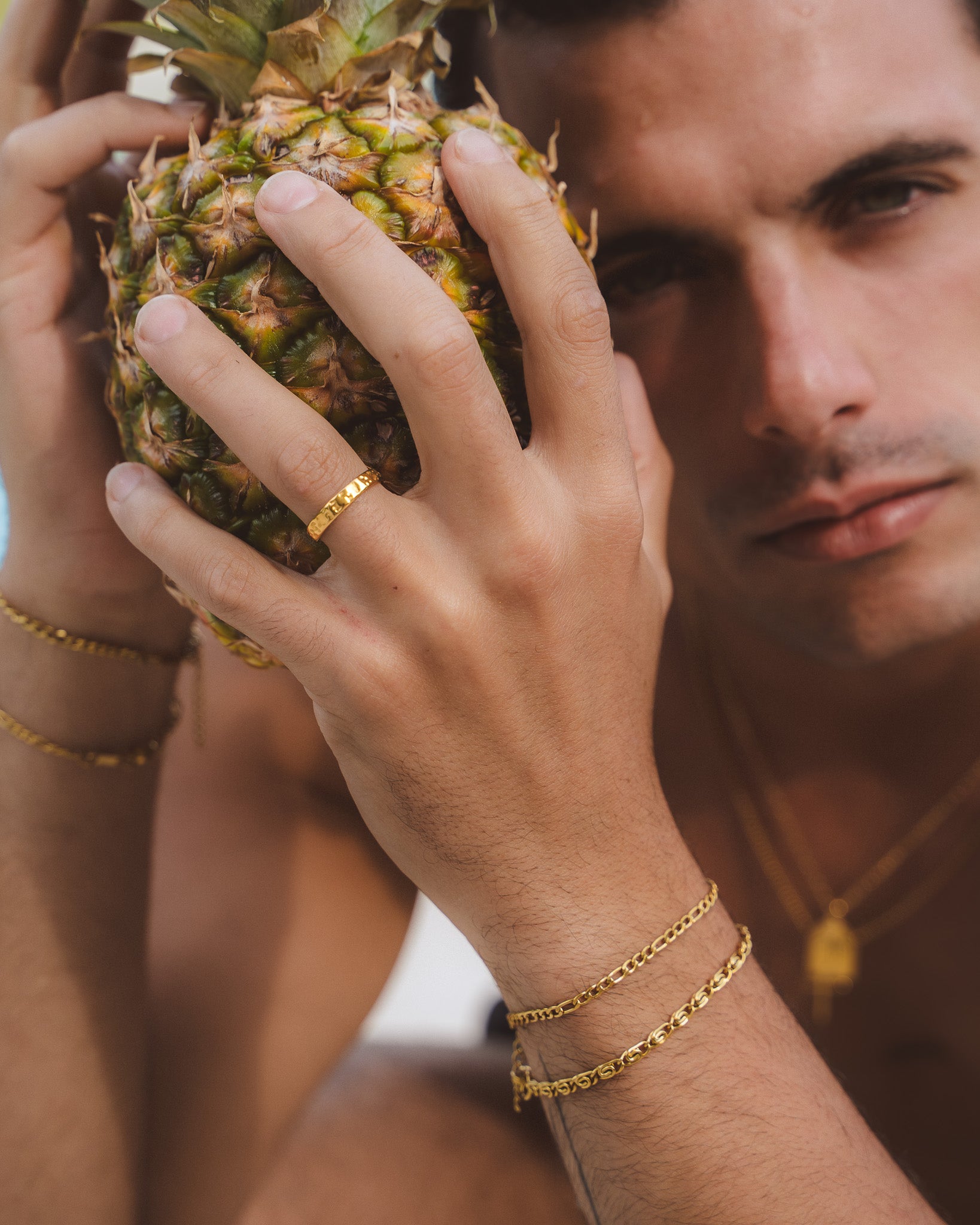 Hammered gold ring on finger held near a pineapple
