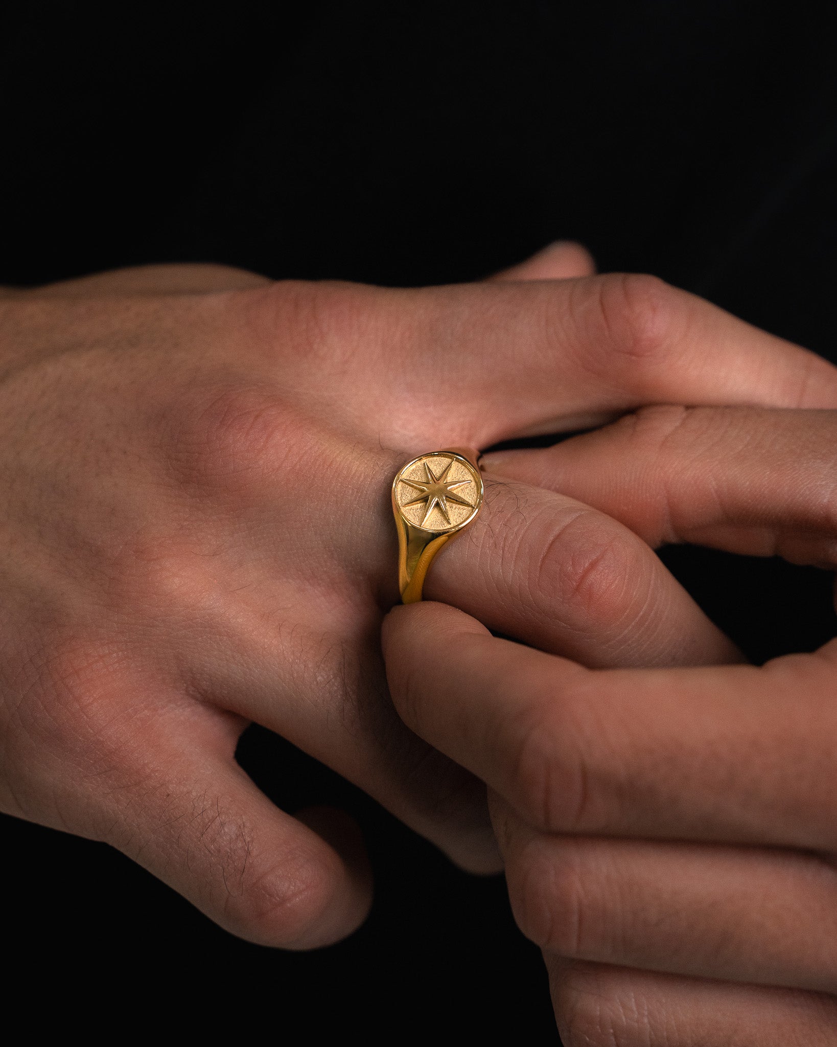 Gold ring with a star motif on a finger against a dark background