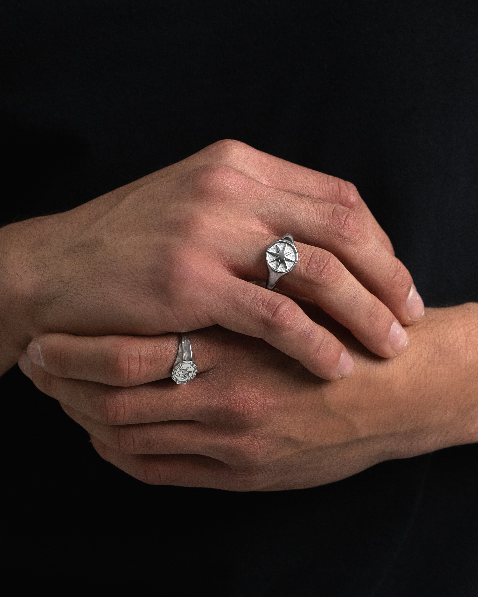 Two silver rings worn on the hand, one with an octagonal crest and the other with a circular symbol