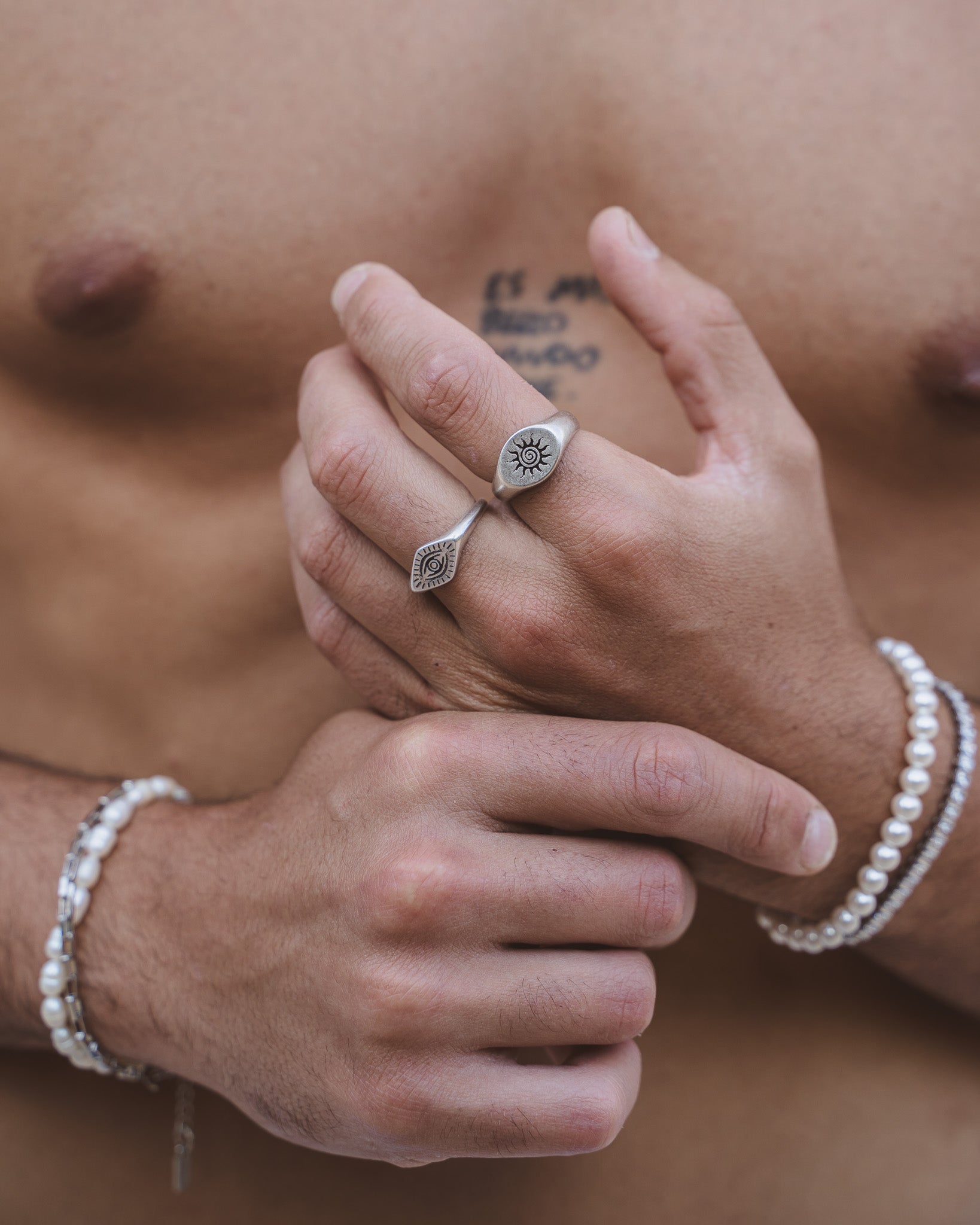 Eye motif ORUS ring on finger with pearl bracelet visible in the background.