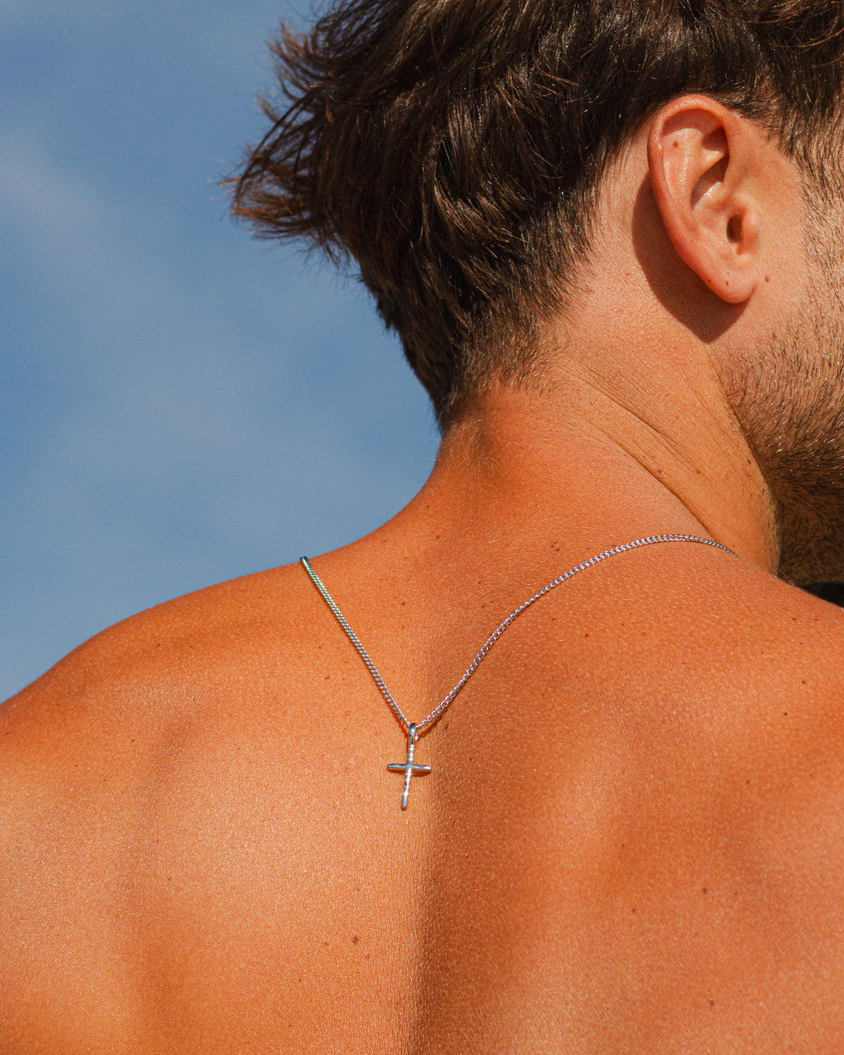 Silver cross necklace on a man with a blue sky background