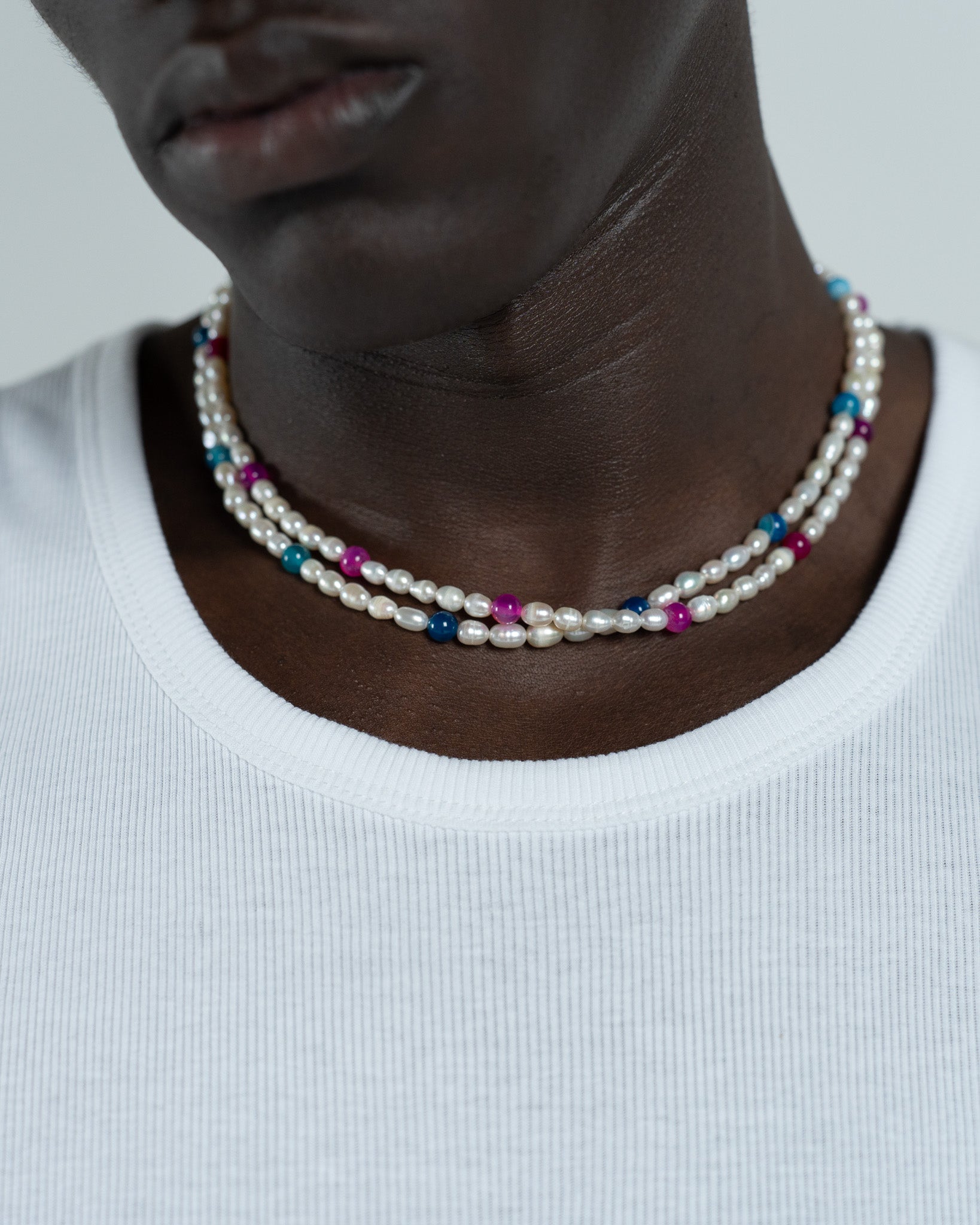 Layered pearl necklace with cream freshwater pearls and colorful beads worn on a white top.