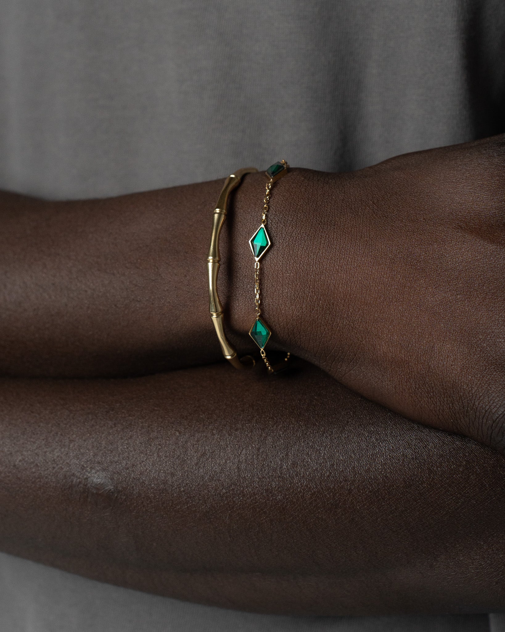 Gold bamboo bracelet paired with a delicate green gemstone bracelet on a dark skinned wrist