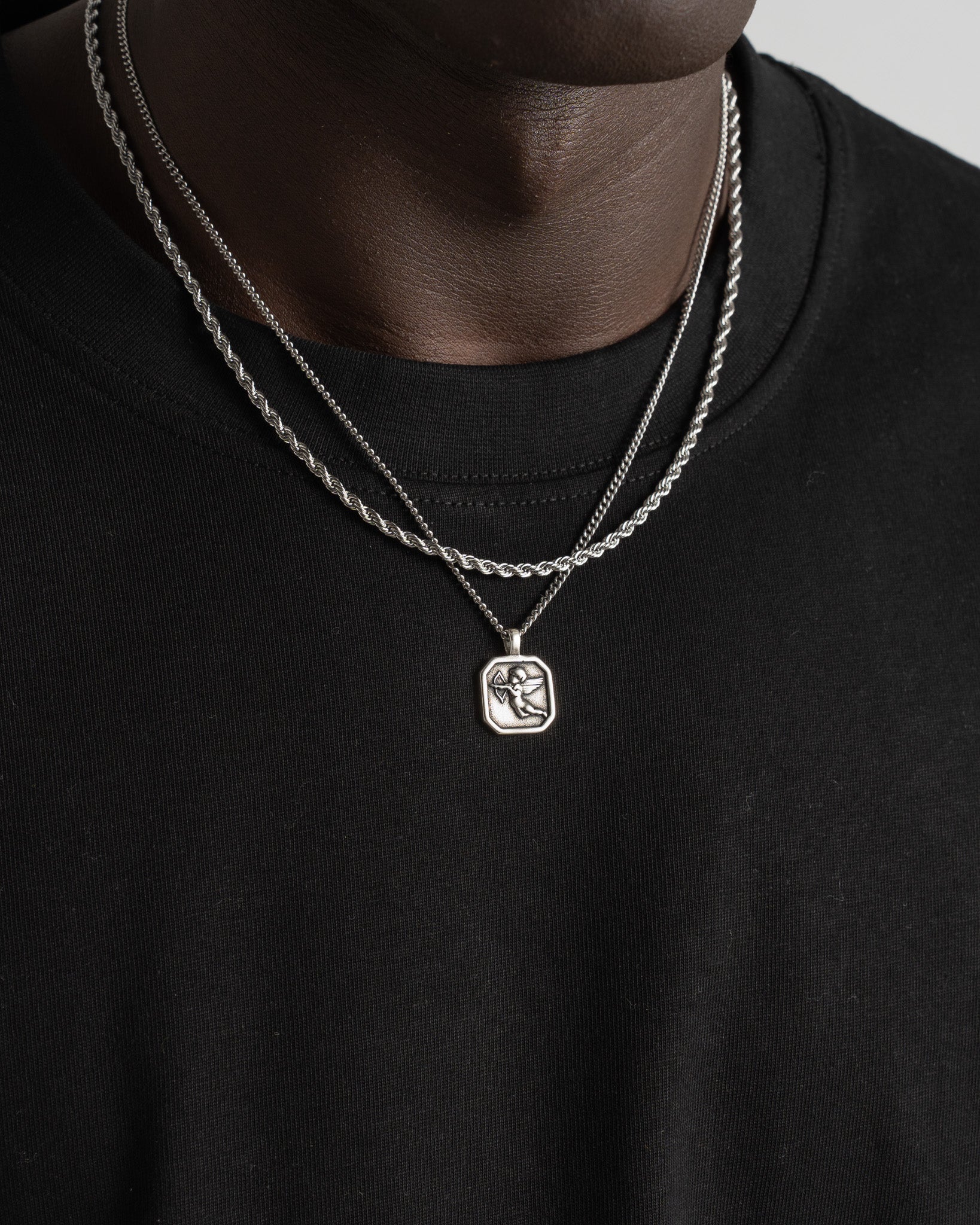 Closeup of Lazio silver 3 mm rope chain layered with another chain on a model wearing a black shirt