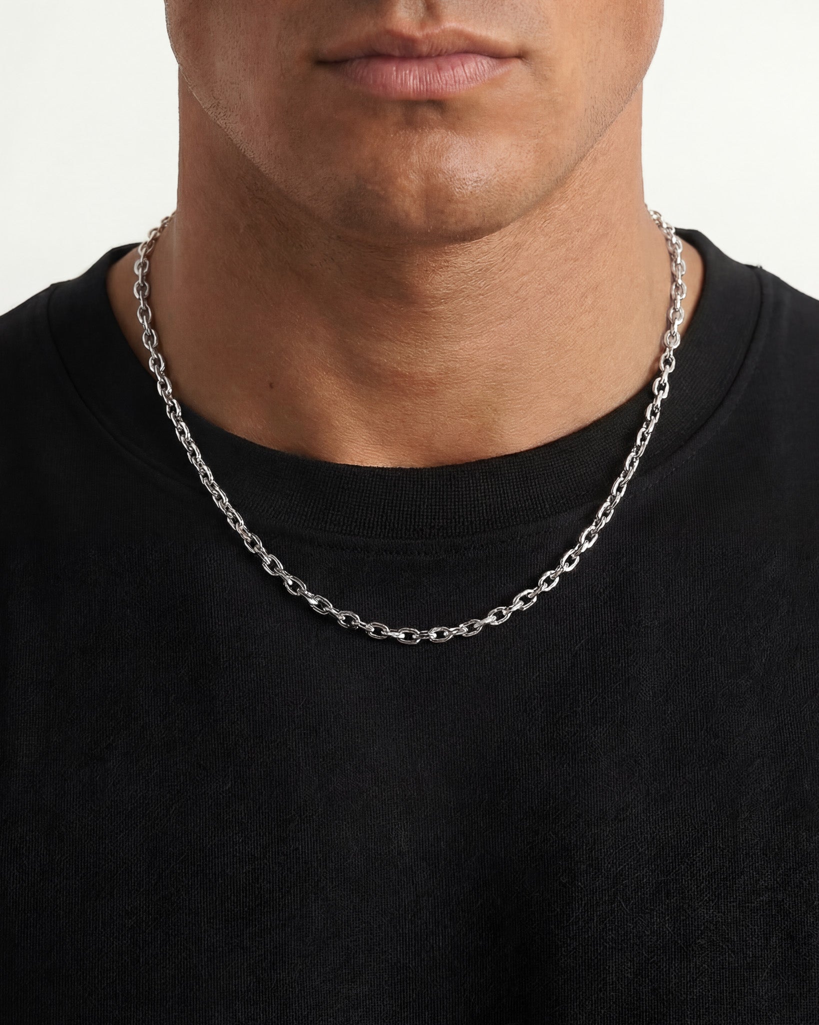 Close up of a silver anchor chain around a man's neck over a black shirt