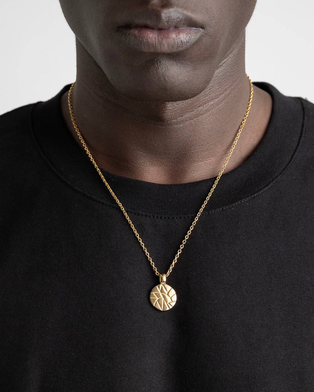 Gold chain necklace with a round geometric pendant worn on a black top.