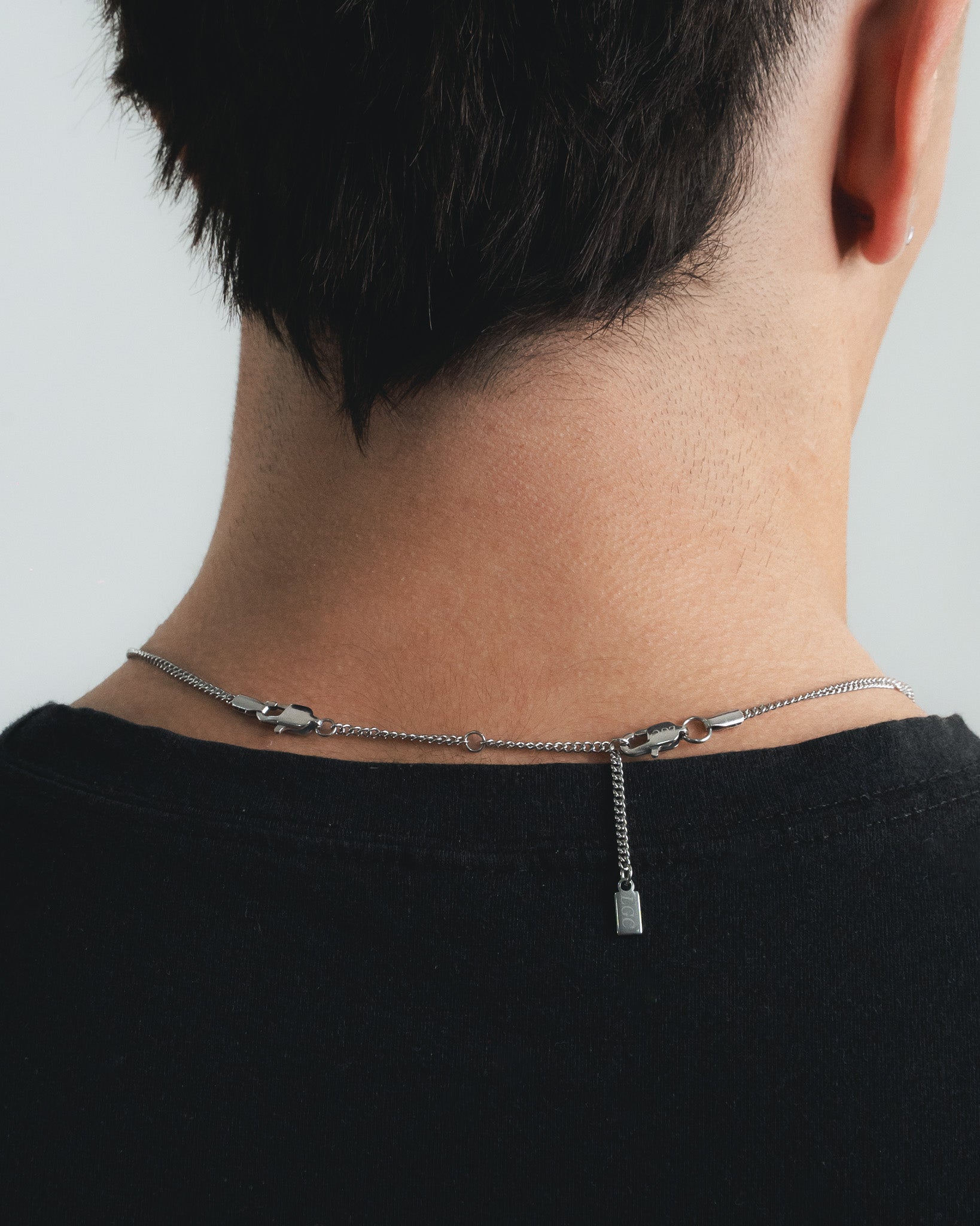 Back of the neck with a silver chain and extender and a small rectangular pendant visible