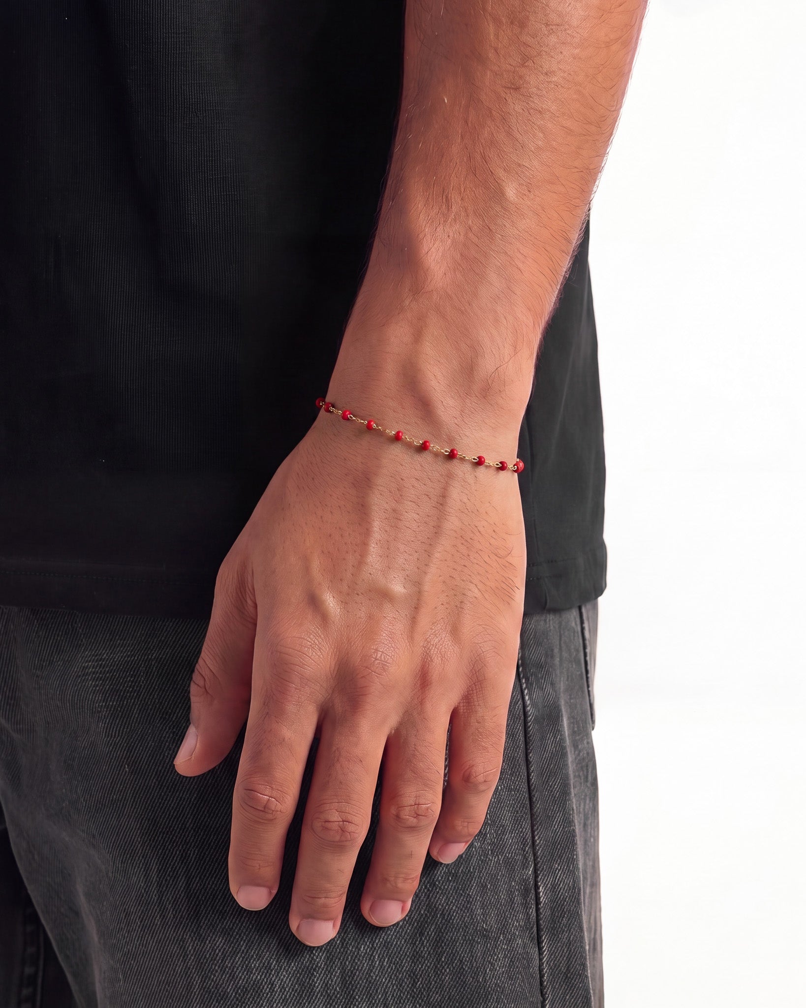 Side view of a gold bracelet with red beads worn on the wrist
