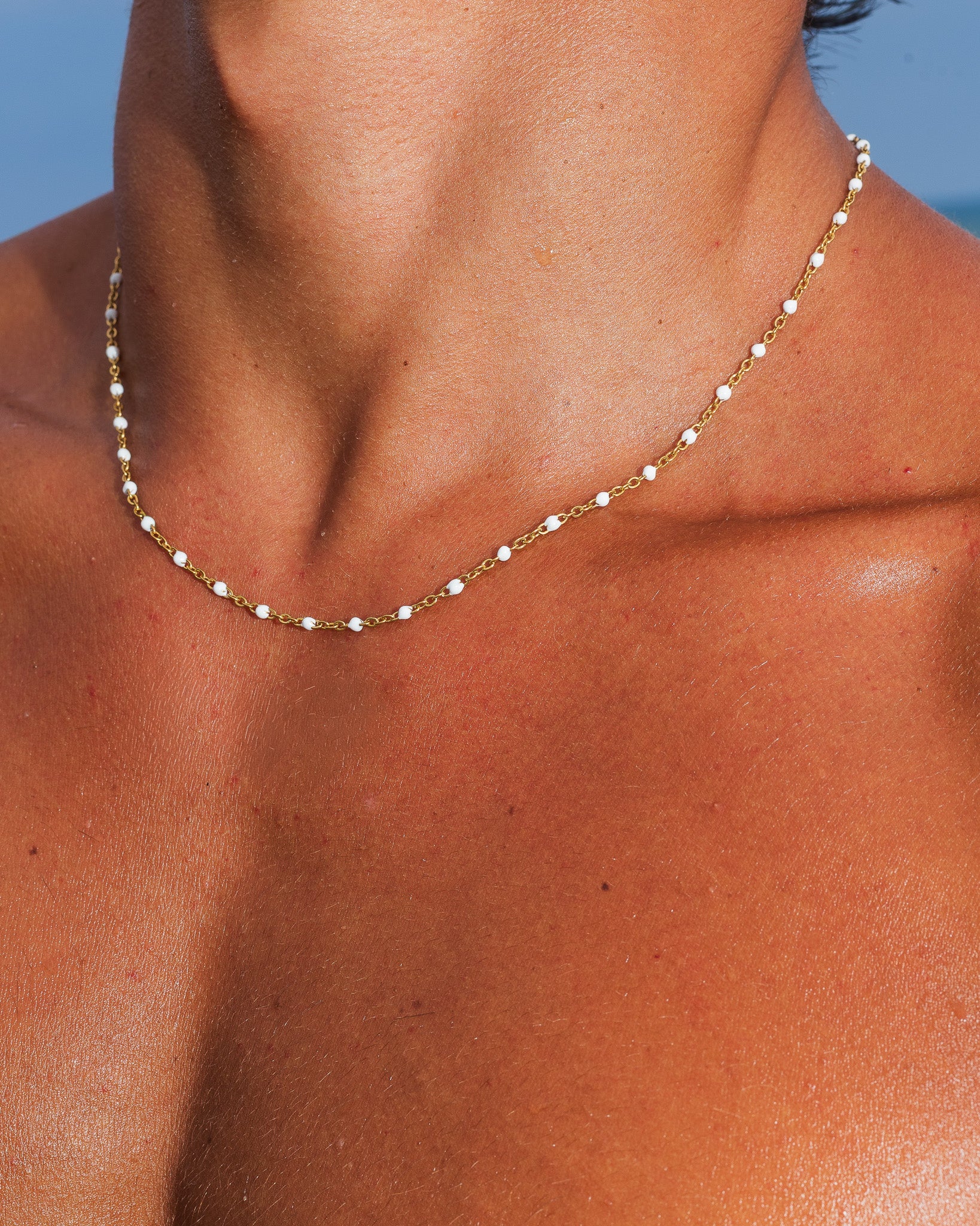Gold chain with white beads drapes along the neck and collarbone.