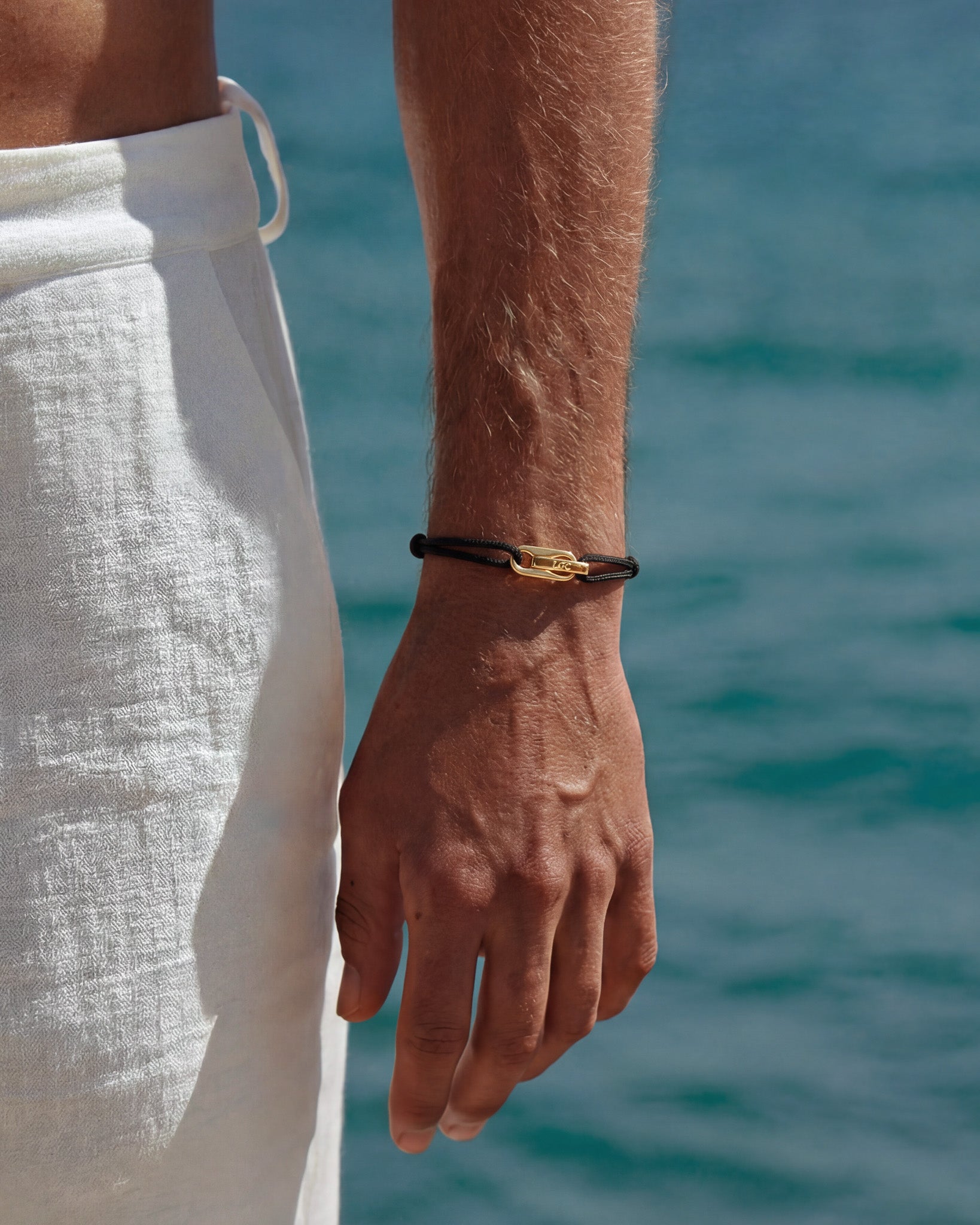 Red cord Atlantis bracelet with gold clasp worn on the wrist by the sea