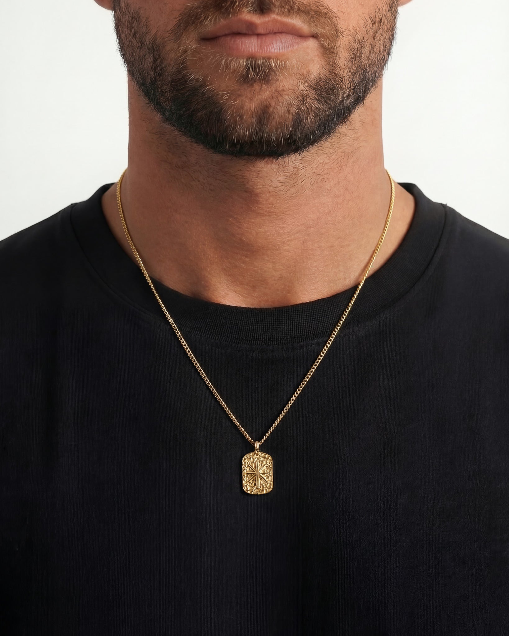 Gold IBZ necklaces on a man featuring a textured rectangular pendant and a circular black inset pendant