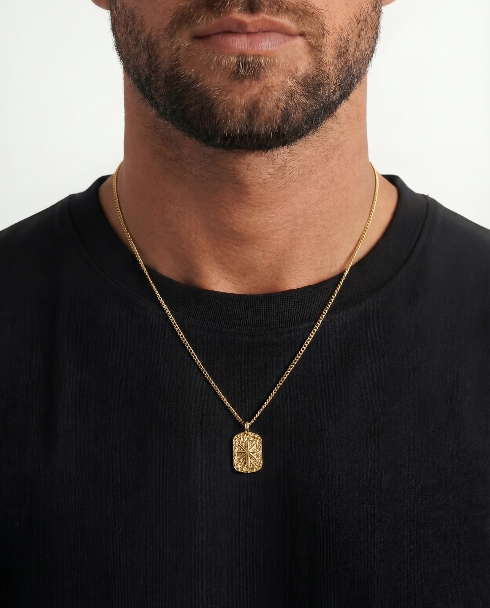 Gold IBZ necklaces on a man featuring a textured rectangular pendant and a circular black inset pendant