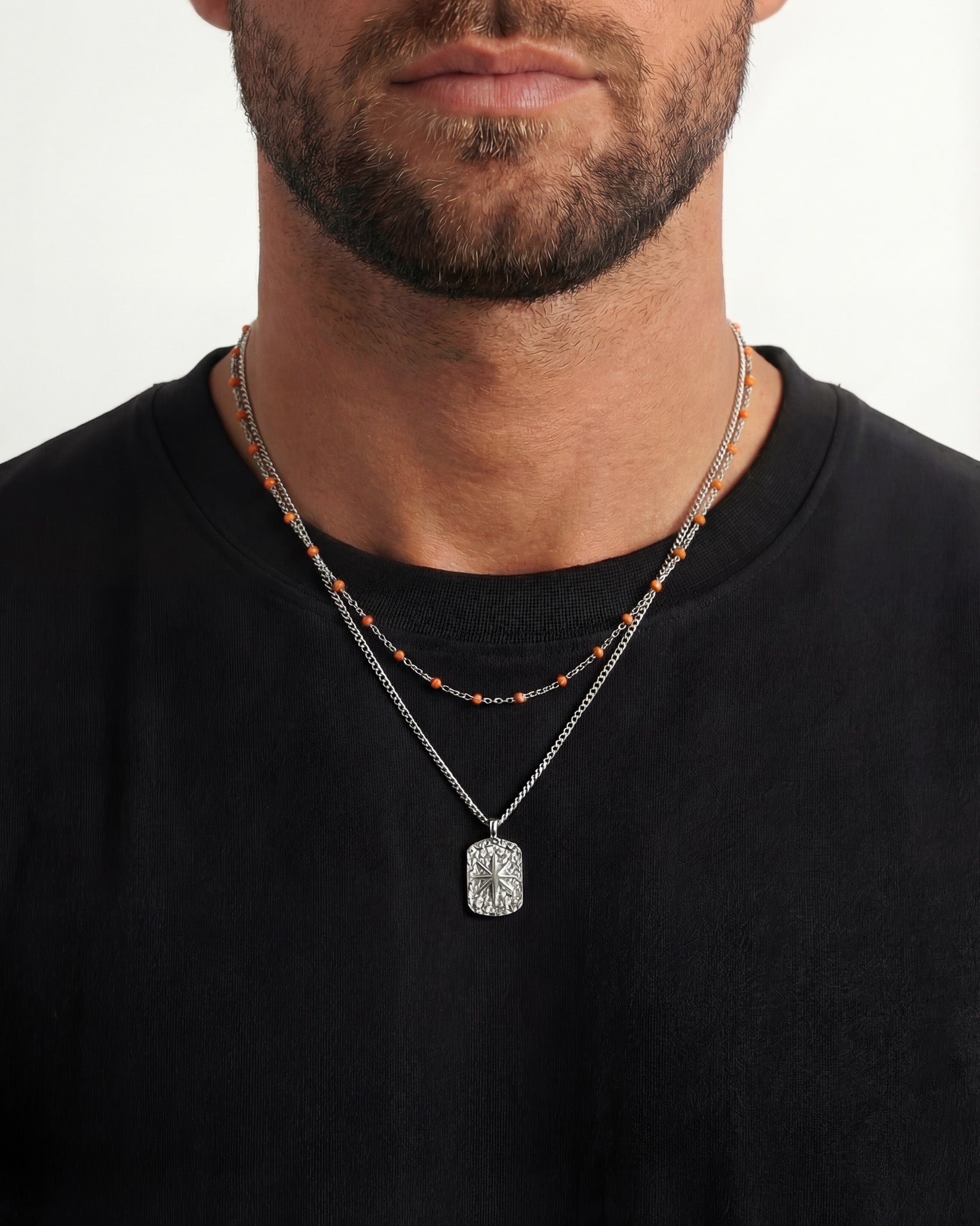 Ibiza inspired layered silver necklace with orange beads and a textured rectangular pendant on a black shirt