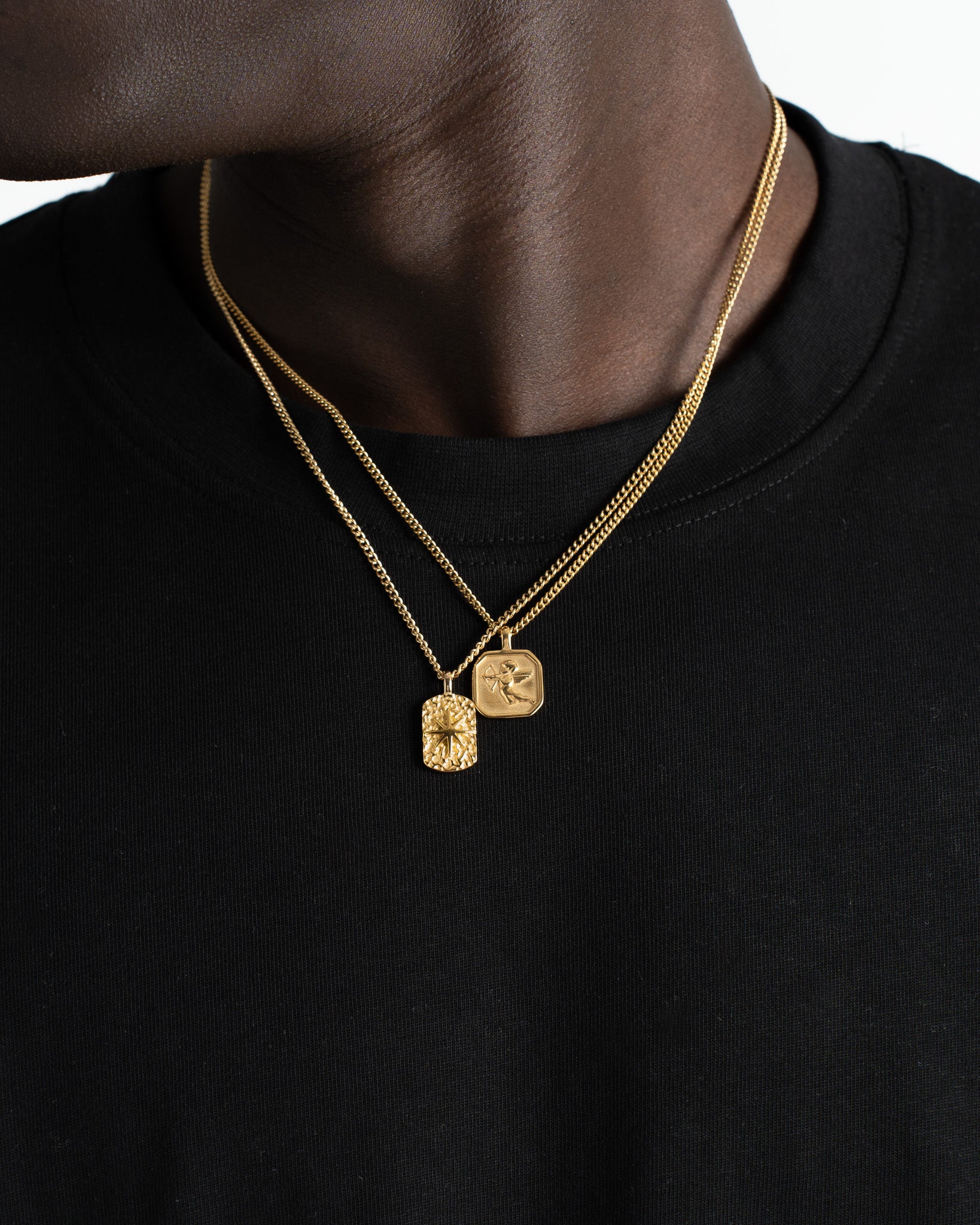 Layered gold chains with two square pendants resting on a model's bare chest