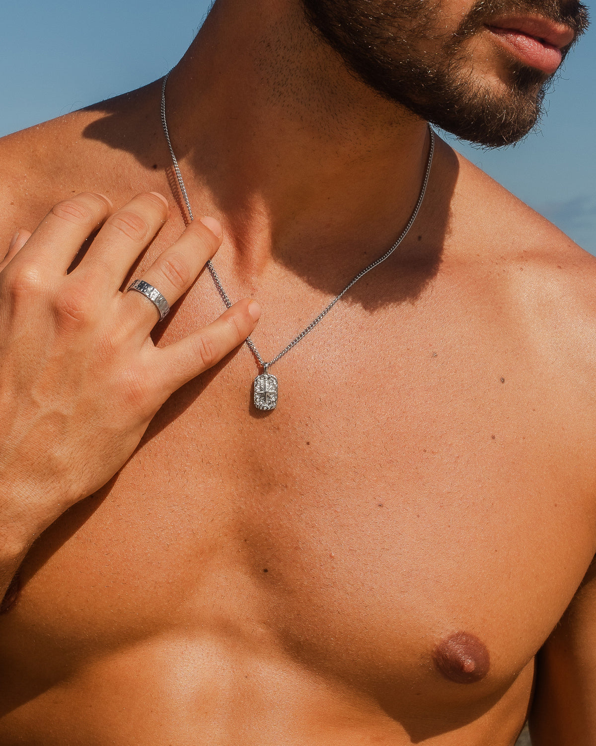 Man wearing a silver IBZ necklace with an ornate rectangular pendant outdoors.