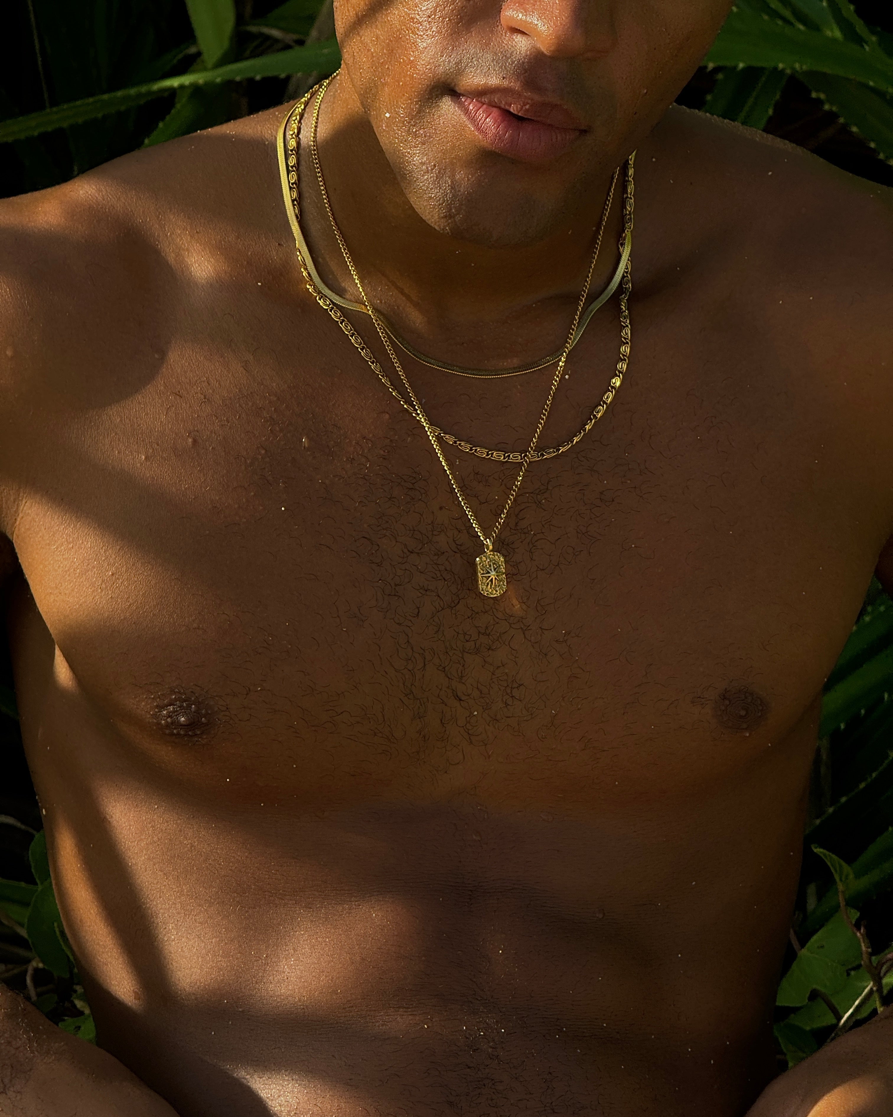 Portrait of a man wearing multiple layered gold necklaces at the beach