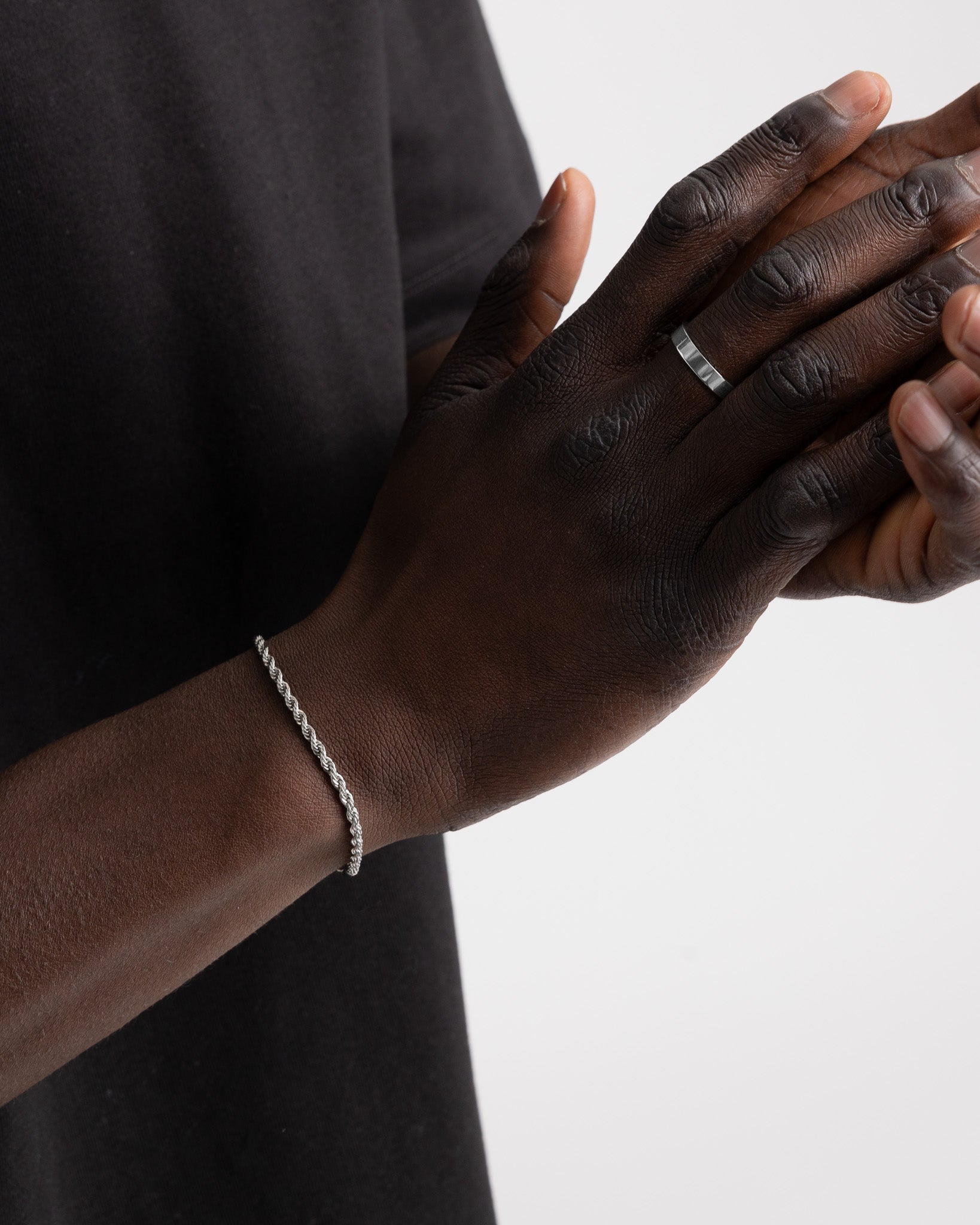 Close up of a dark skinned hand wearing the VERO silver ring on the finger with a silver chain bracelet visible at the wrist