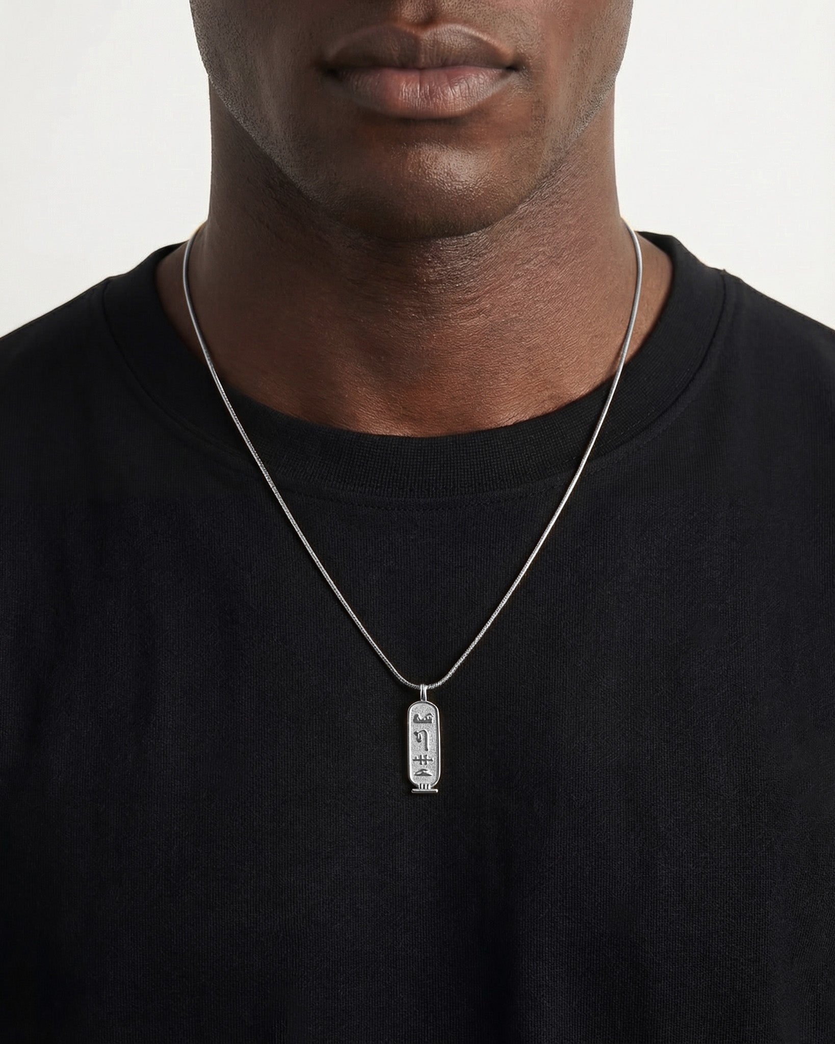 Luxor Silver Necklace pendant with vertical hieroglyphs on a silver chain worn against a black shirt
