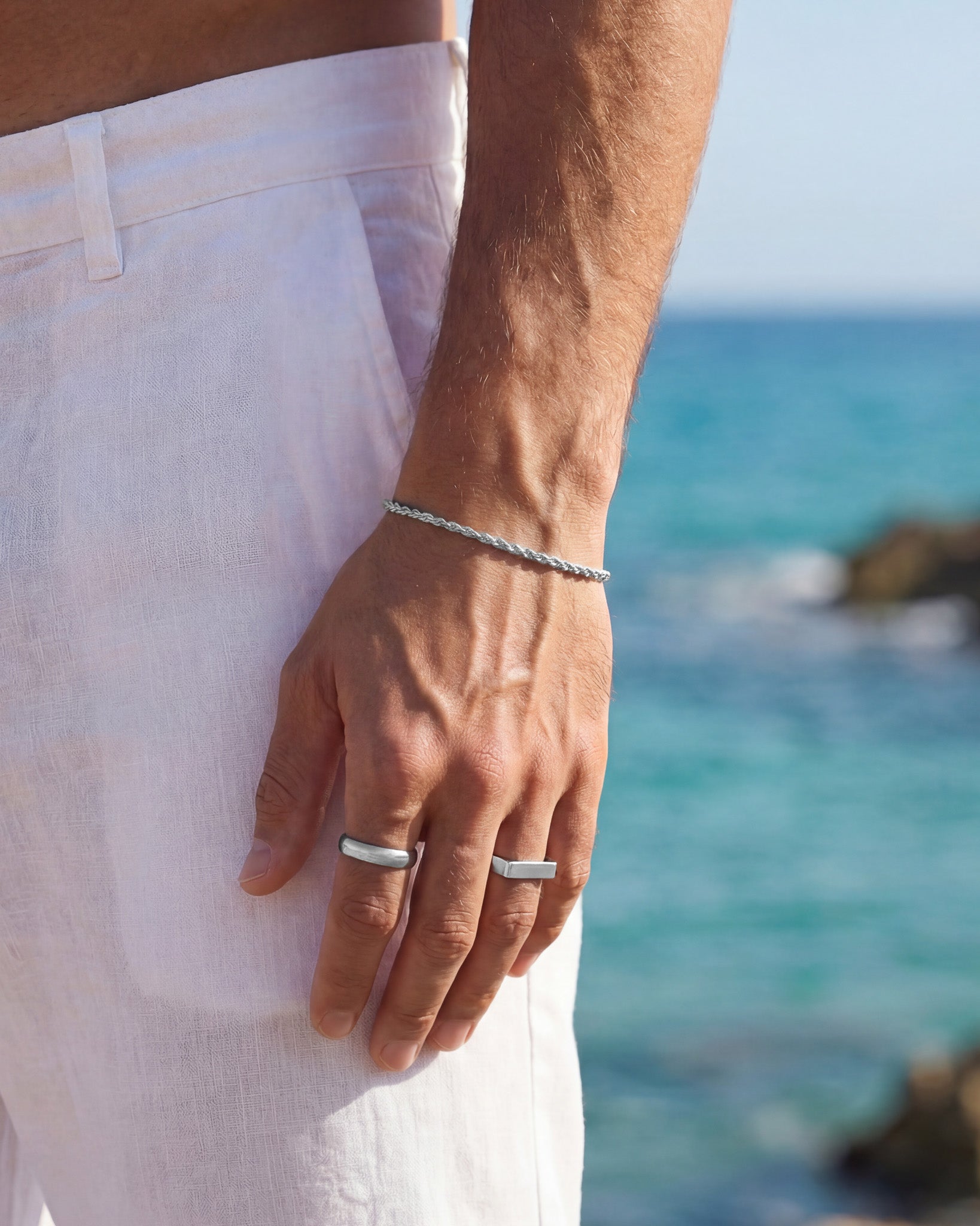 Silver braided chain bracelet on the wrist with a sea backdrop.