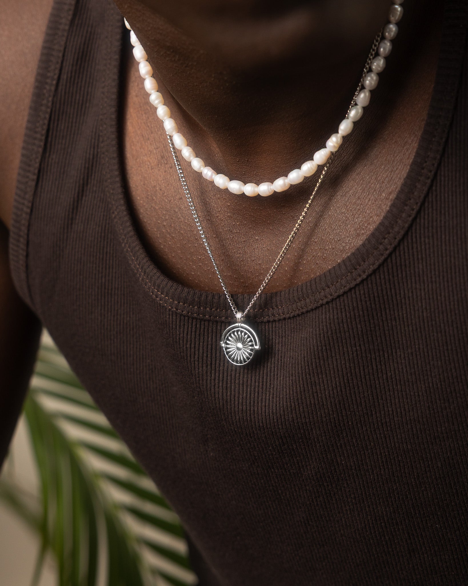 Brown shirted man with a pearl bead Daisy necklace layered with a silver chain and pendant