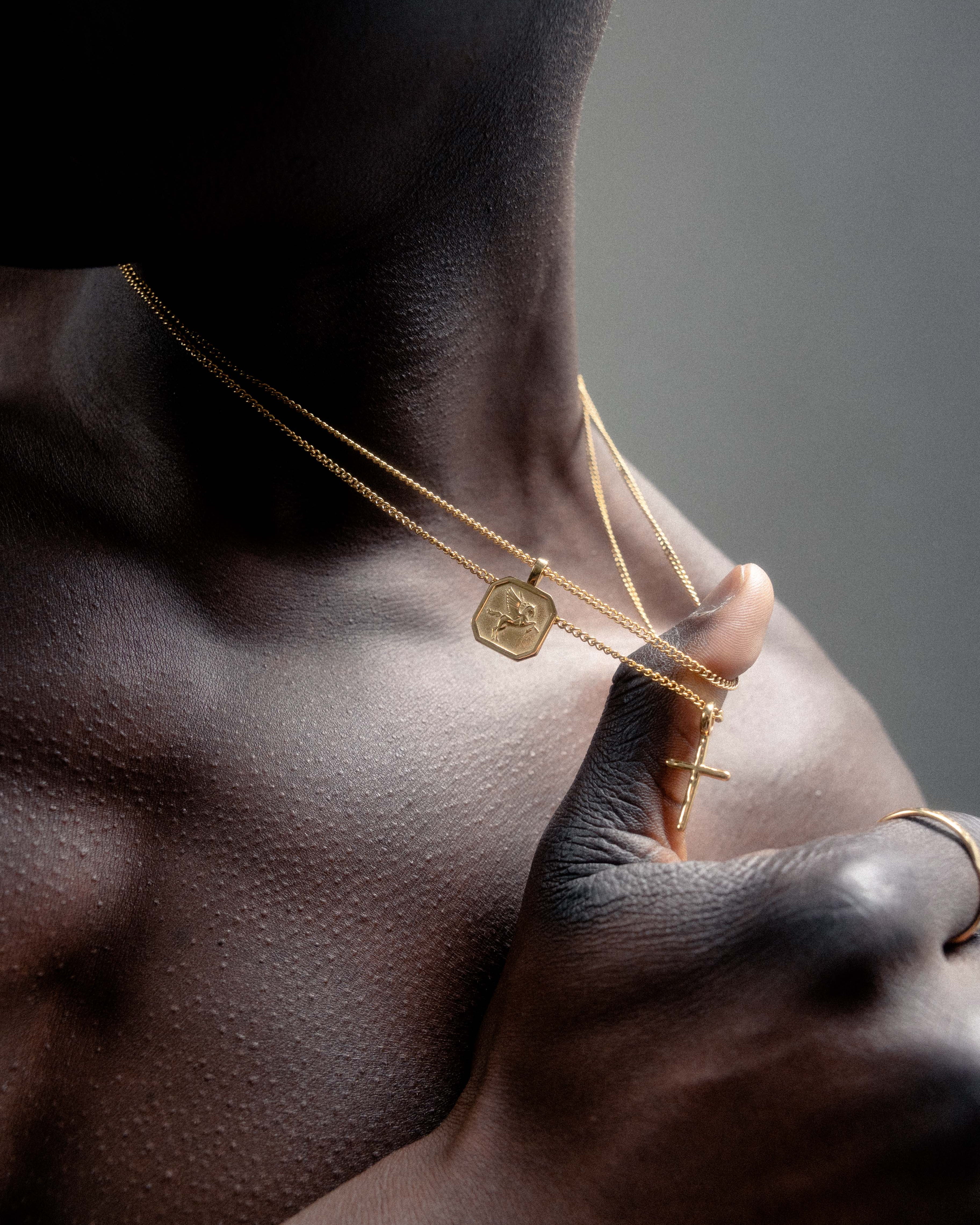 Layered gold Pegasus necklace with a hexagonal pendant resting on a dark-skinned neck.