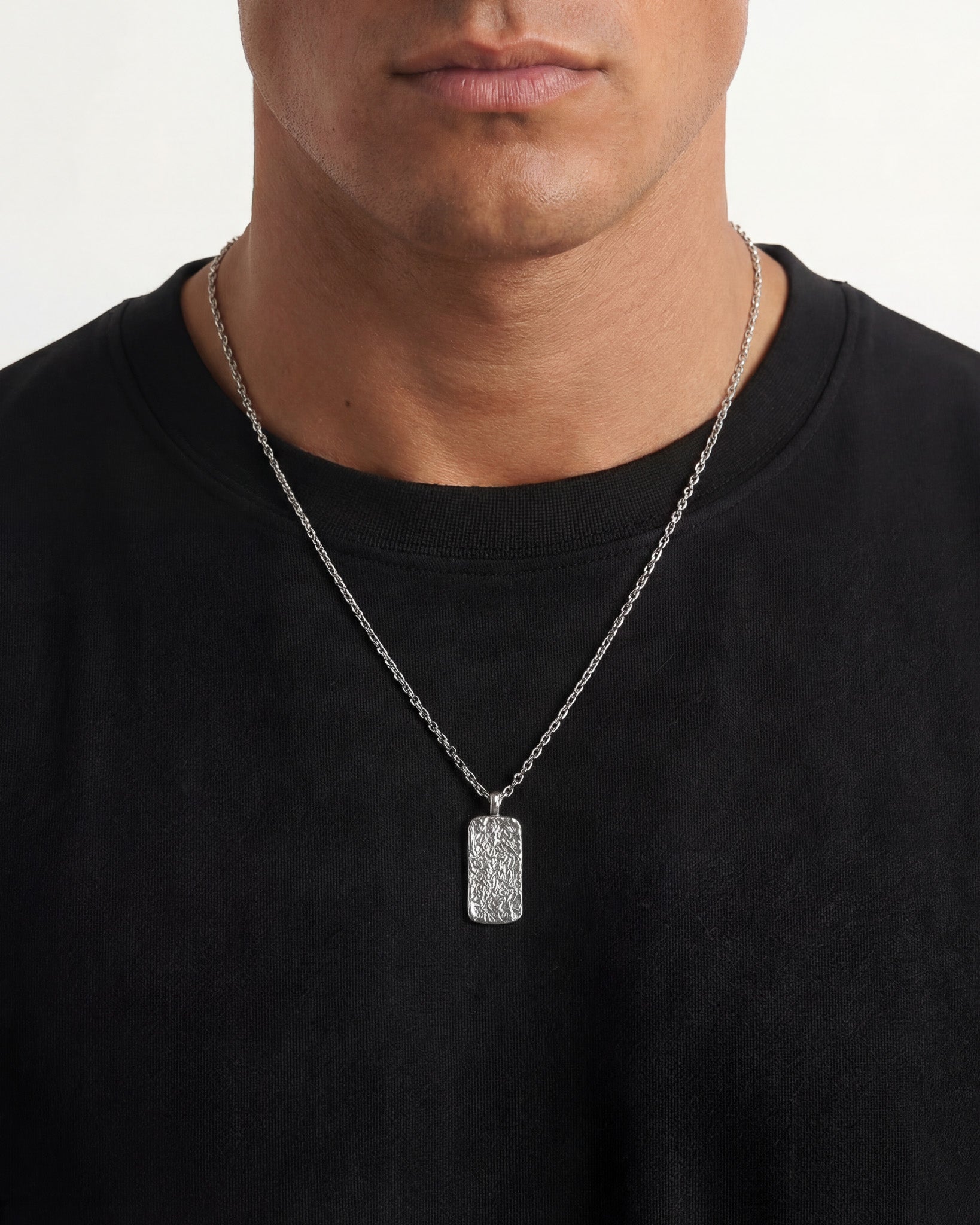 Moonrock silver necklace worn on a man with a black shirt featuring a textured rectangular pendant