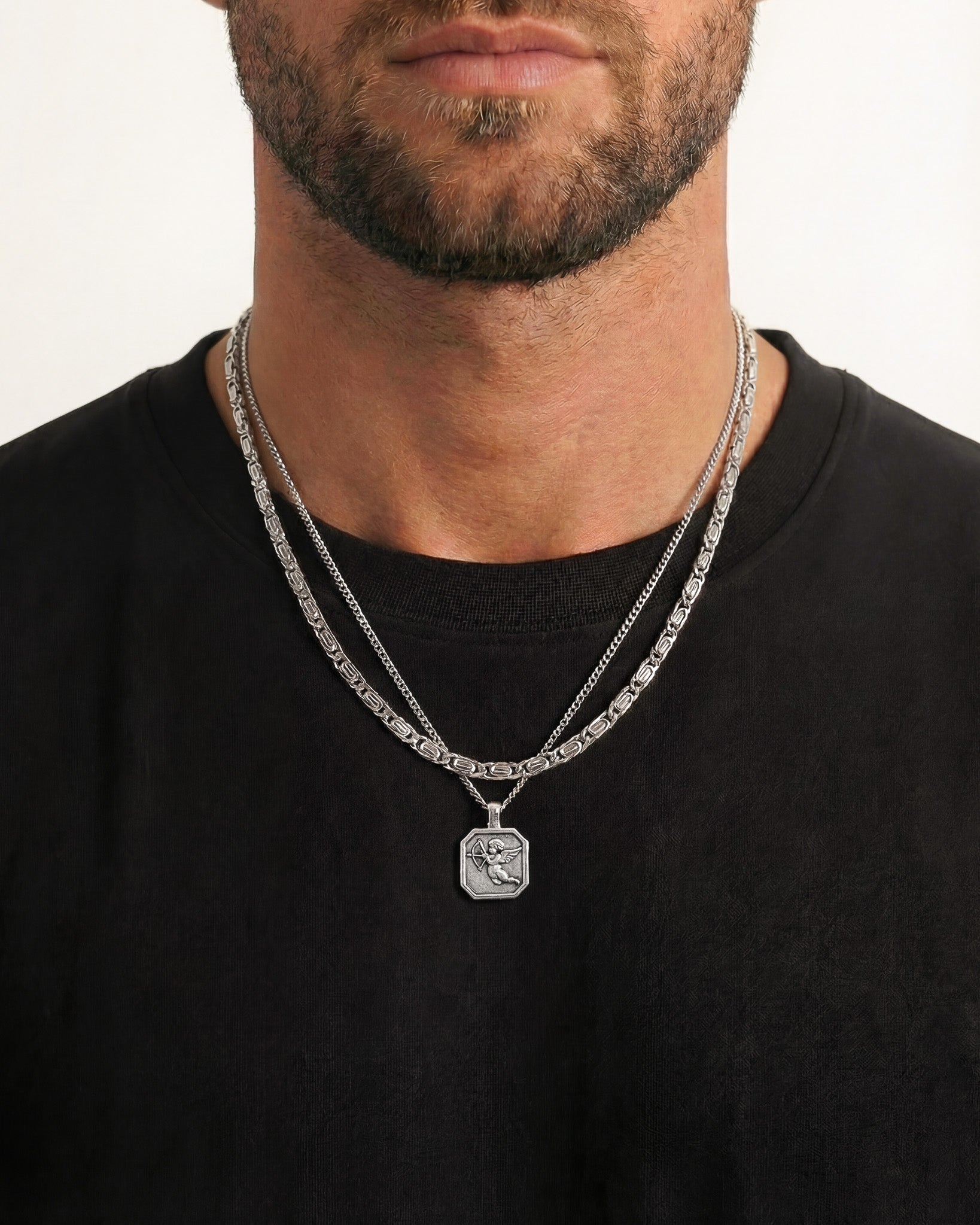 Cupid pendant on an octagonal silver pendant with layered chains resting on the chest.