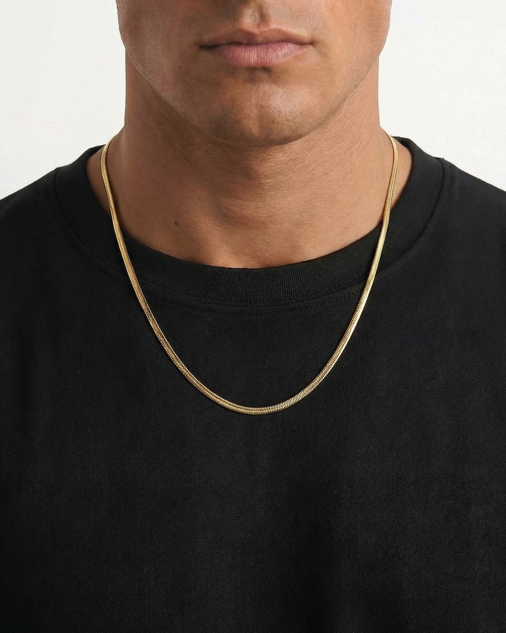 Close up of a wavy gold chain necklace resting on the wearer's neck over a black T shirt