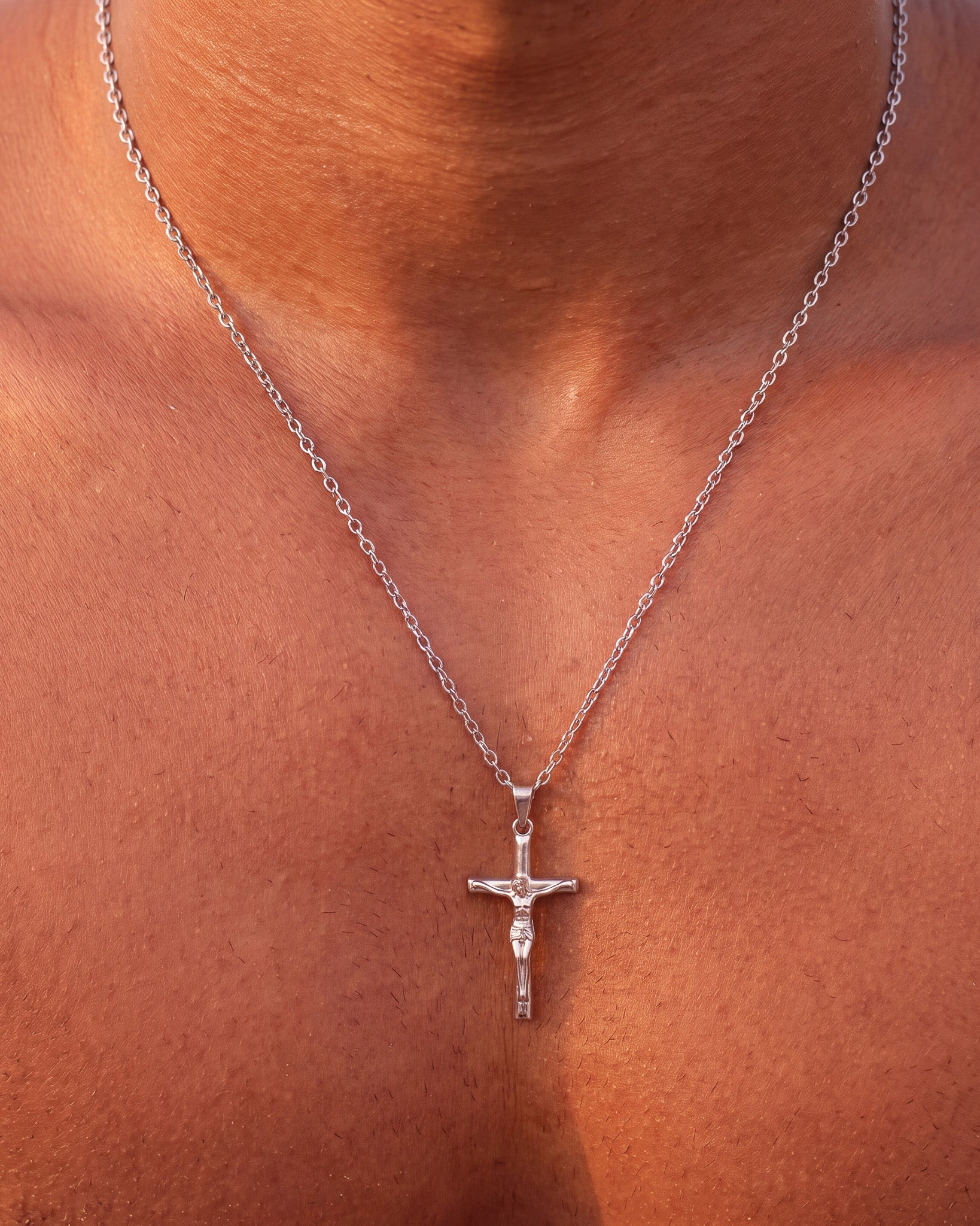 Close up of silver crucifix pendant with chain draped over the chest