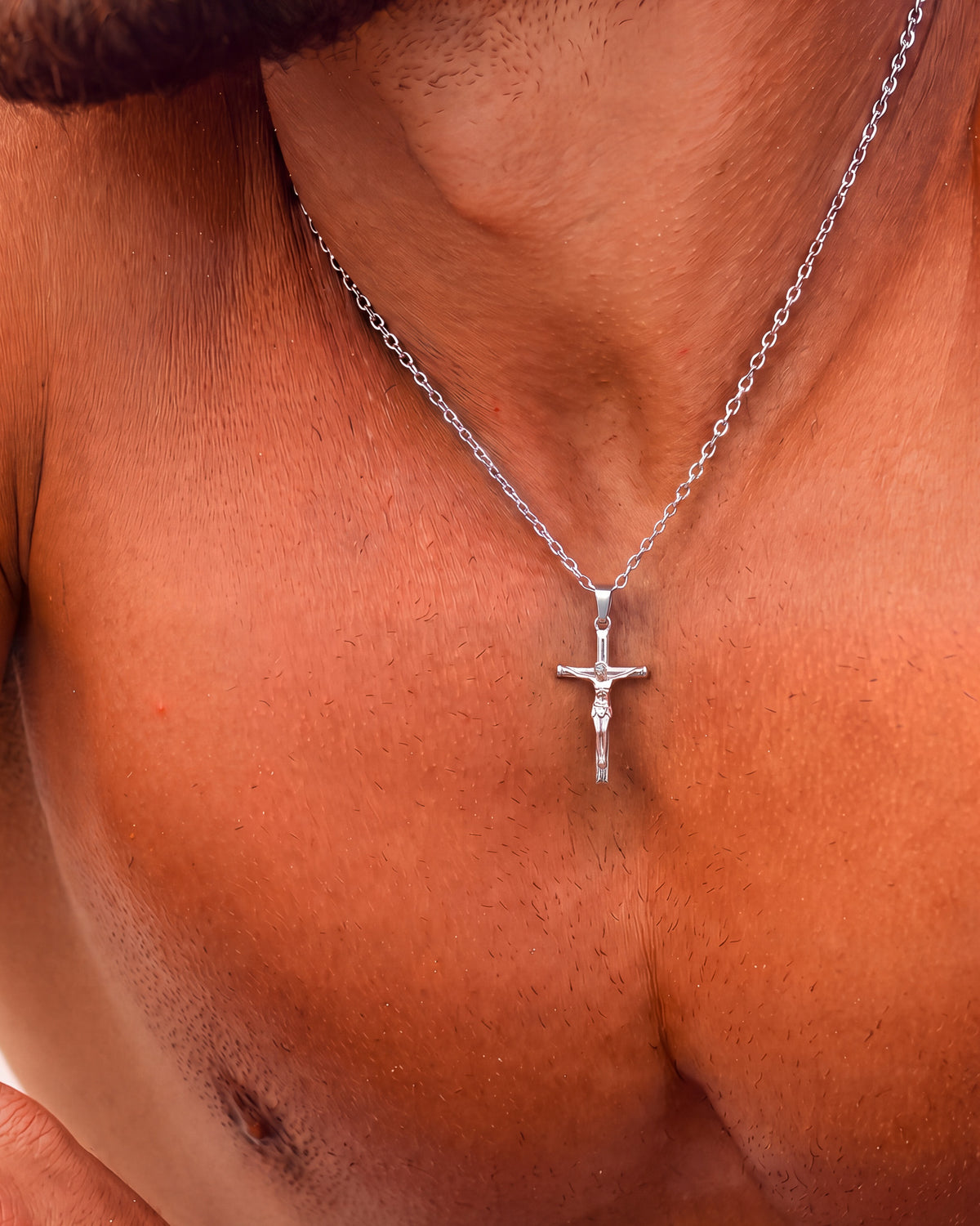 Silver crucifix necklace worn around the neck with pendant resting at the collarbone