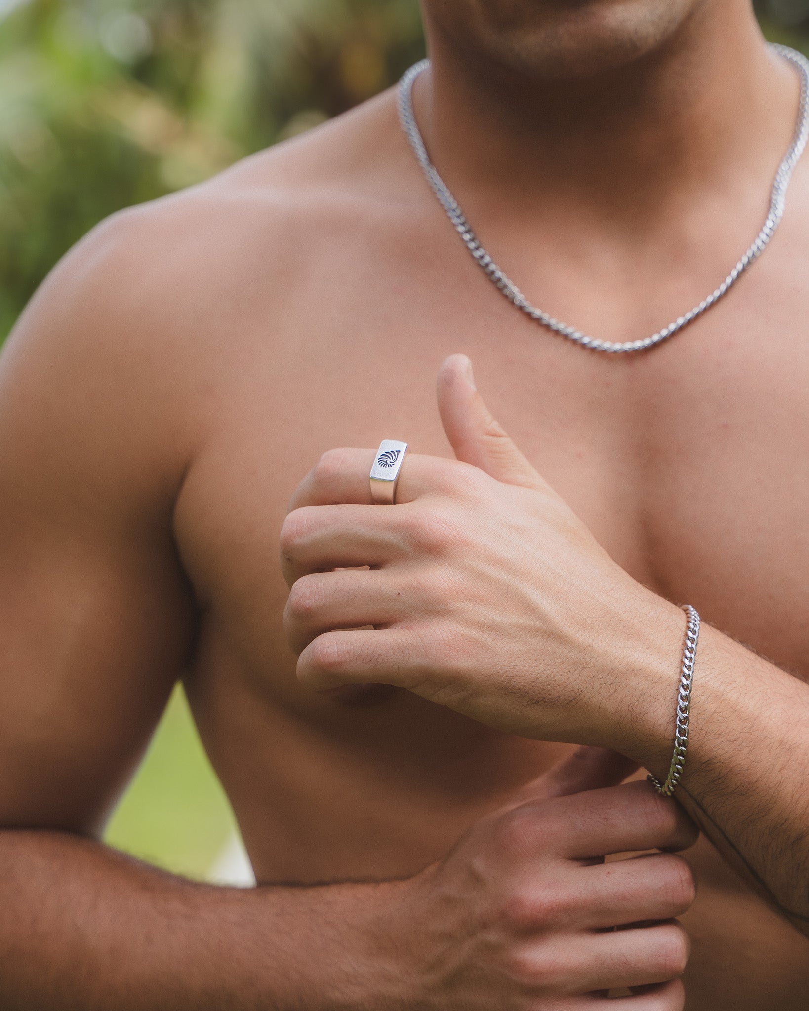 Man wearing a square-faced silver shell ring on his finger and a silver chain necklace.