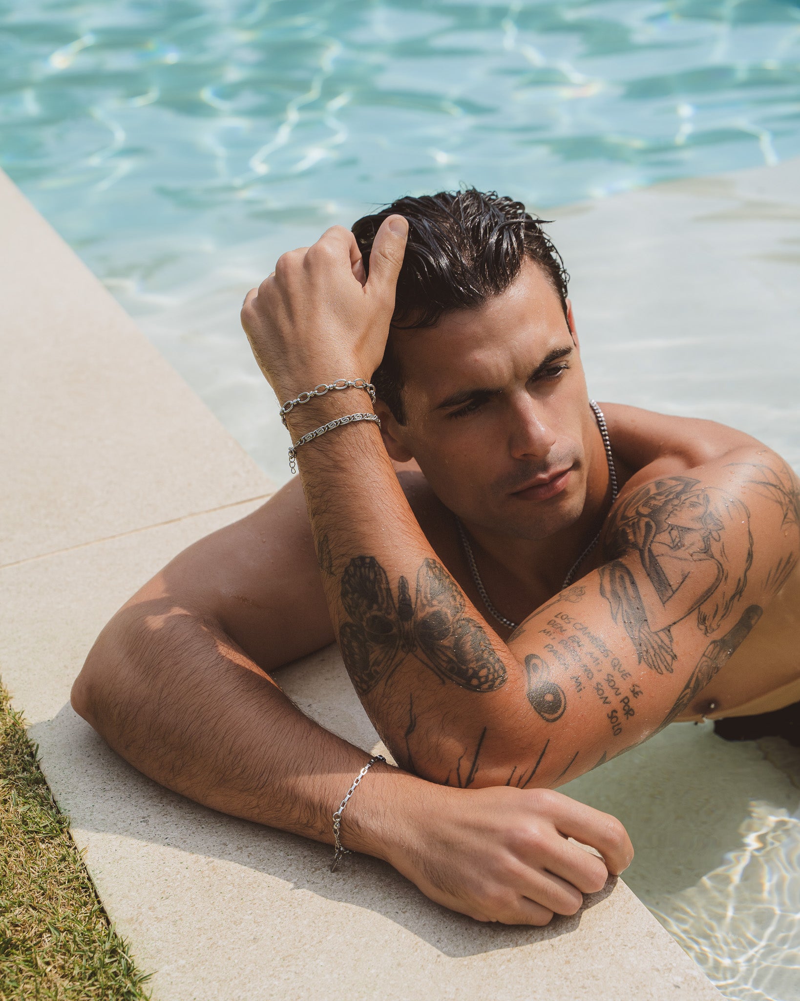 Capri silver bracelet on a man's wrist by the pool with layered bracelets and tattoos