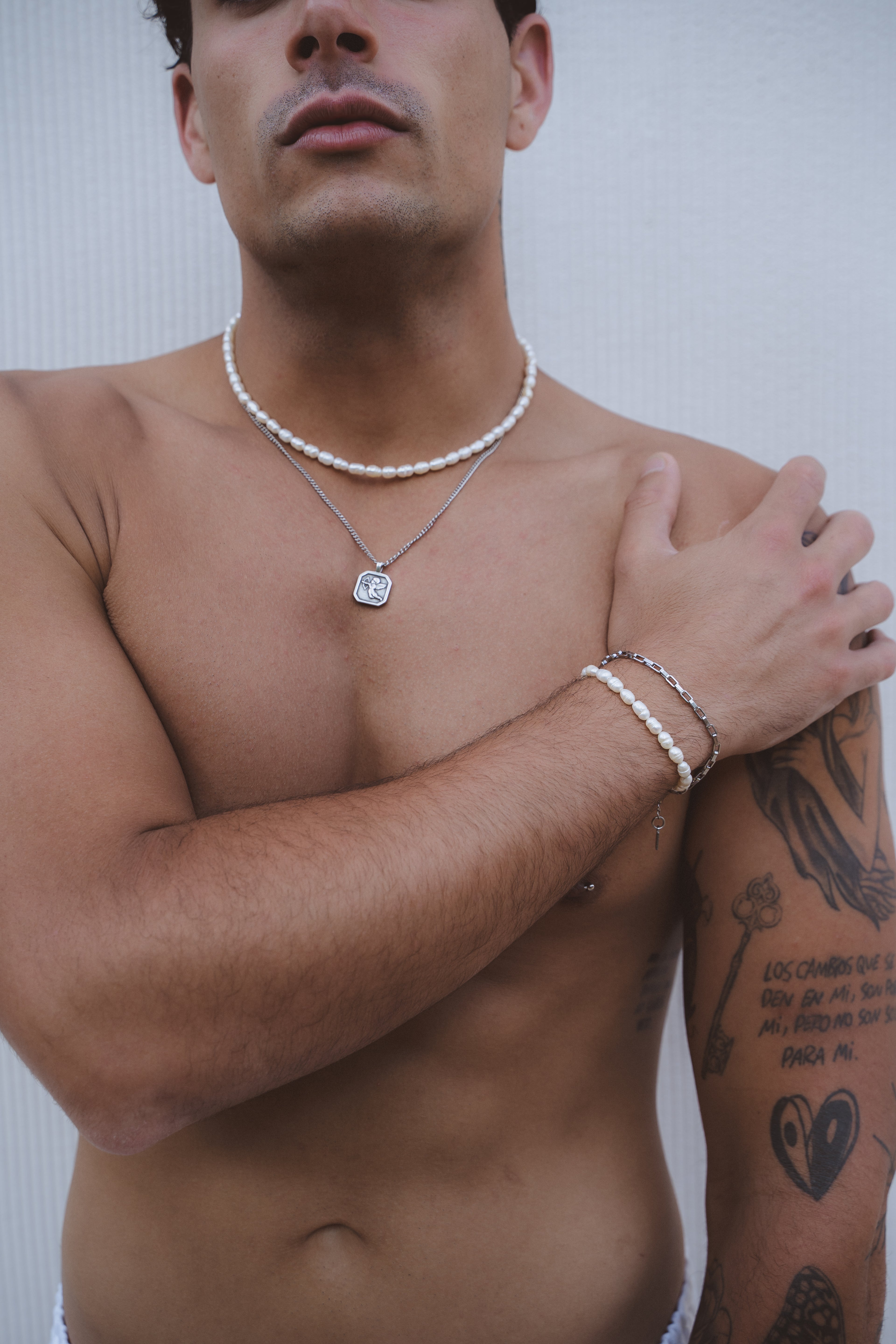 Close-up of a silver Cuban link chain on the bare chest of a tattooed man.