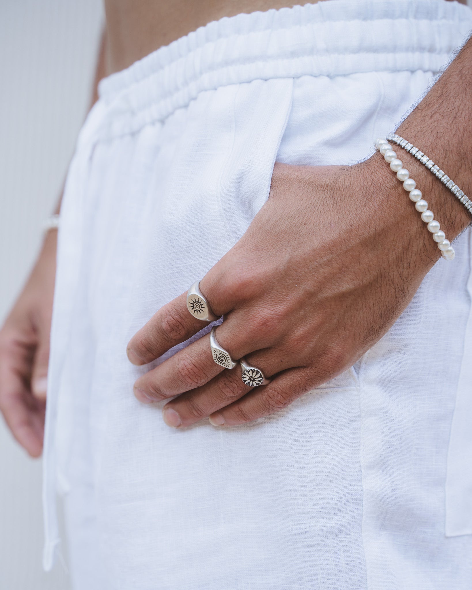 Wrist and hand view showing pearl bracelet and a silver sun emblem ring on the finger with a white shirt backdrop