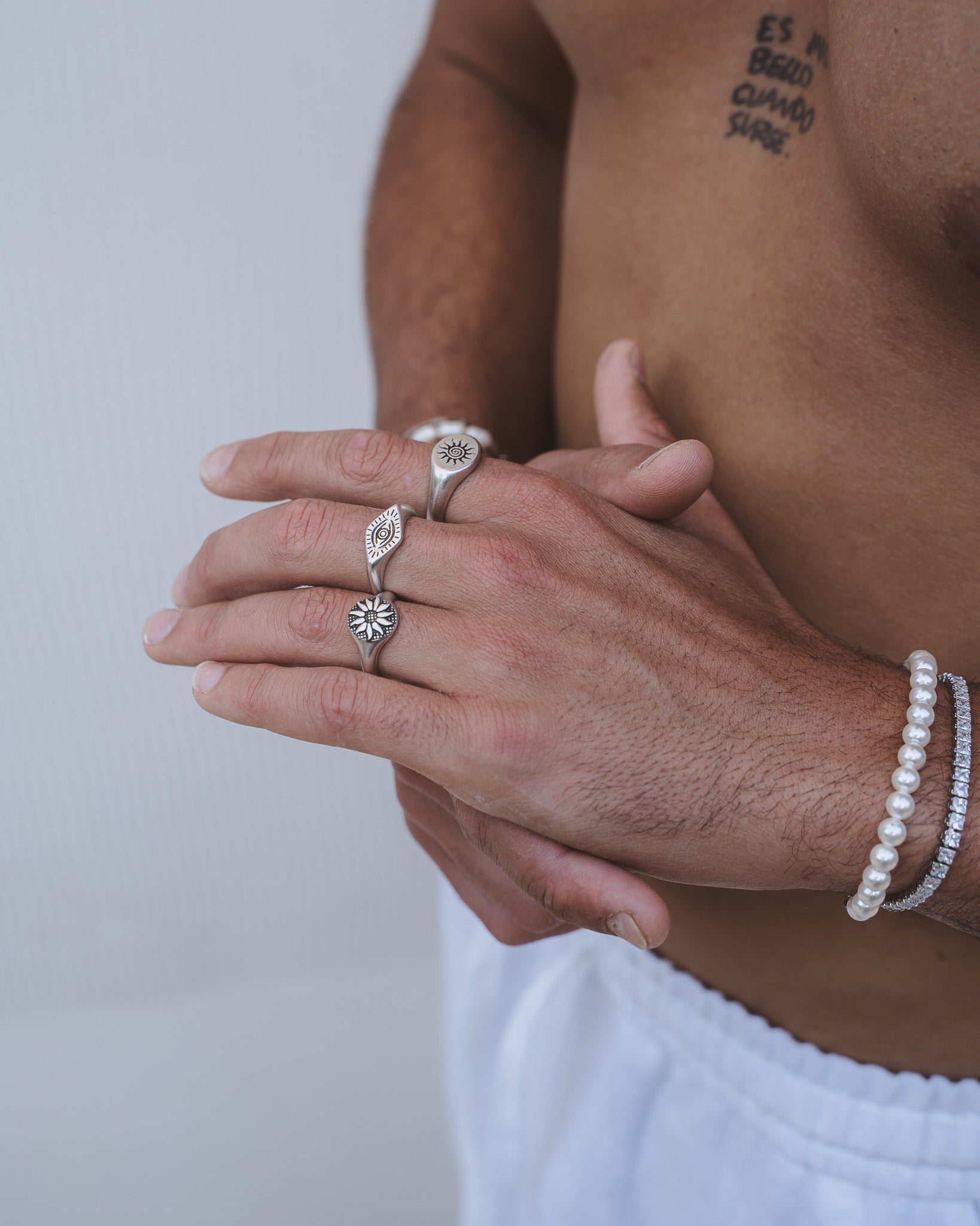 Close up of a hand with several silver rings including eye and sun motifs and a pearl bracelet