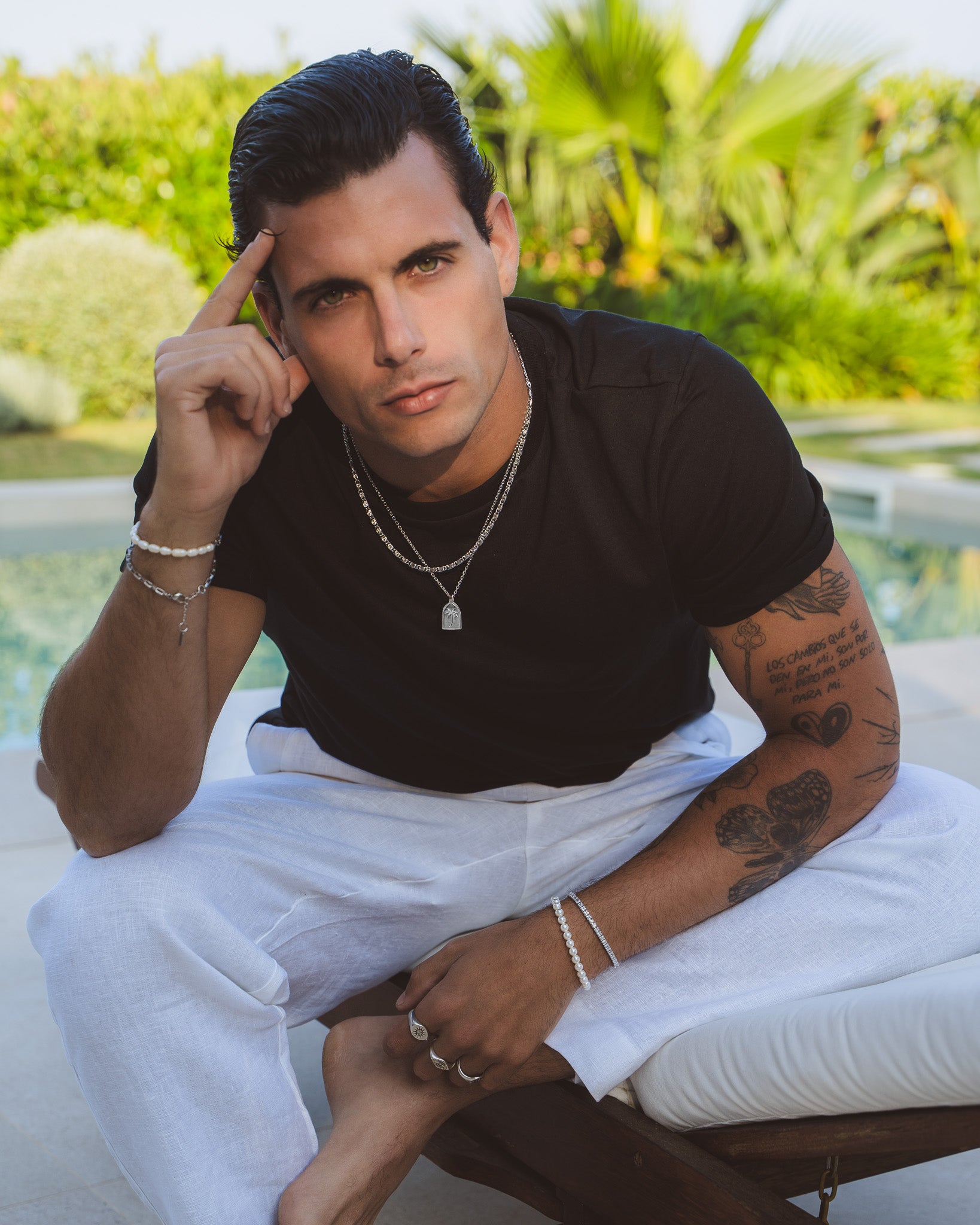 Man with palm tree pendant necklace and layered silver chains in a sunny outdoor setting