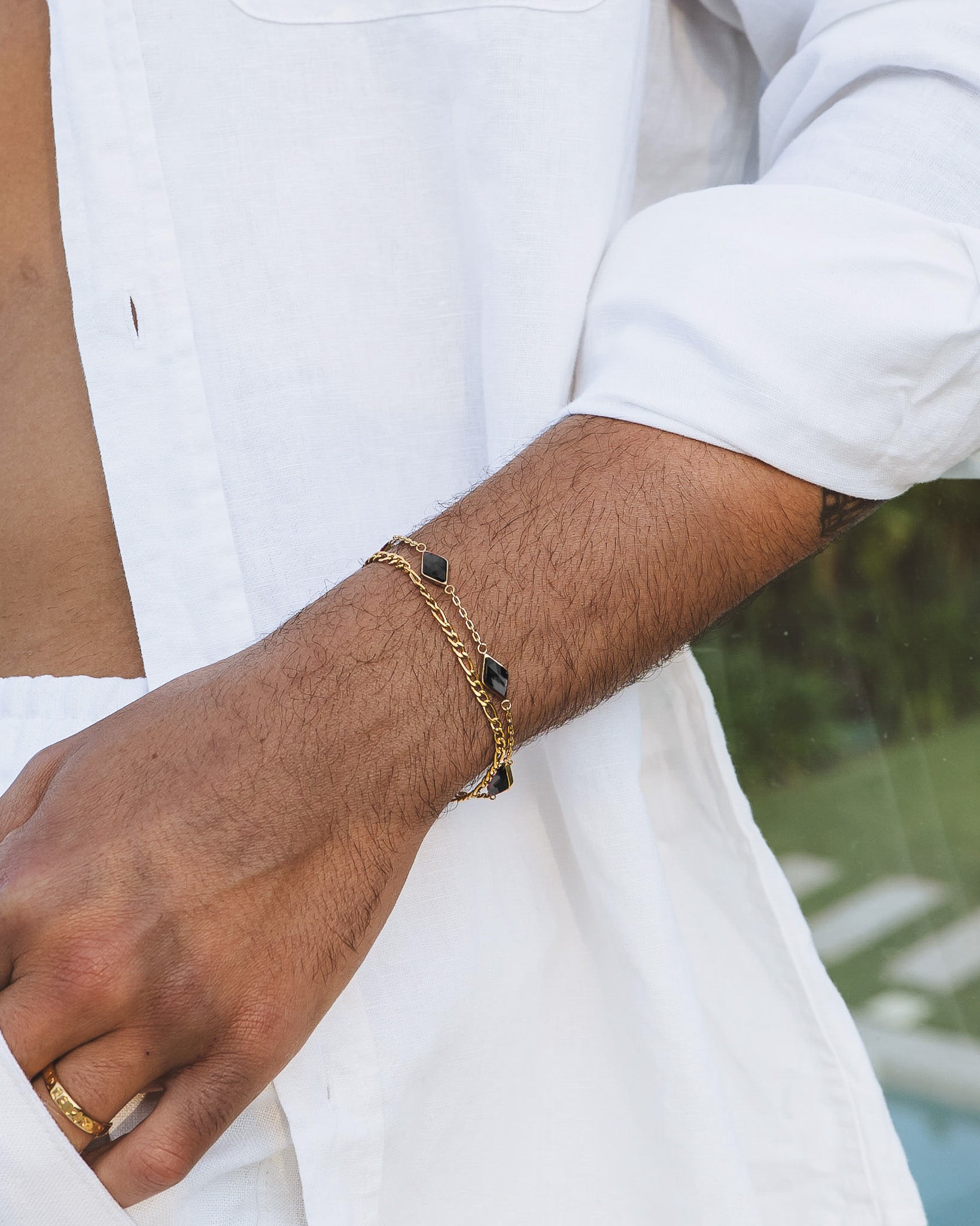 Amberes gold bracelet with square black gemstones on a wrist above a white shirt