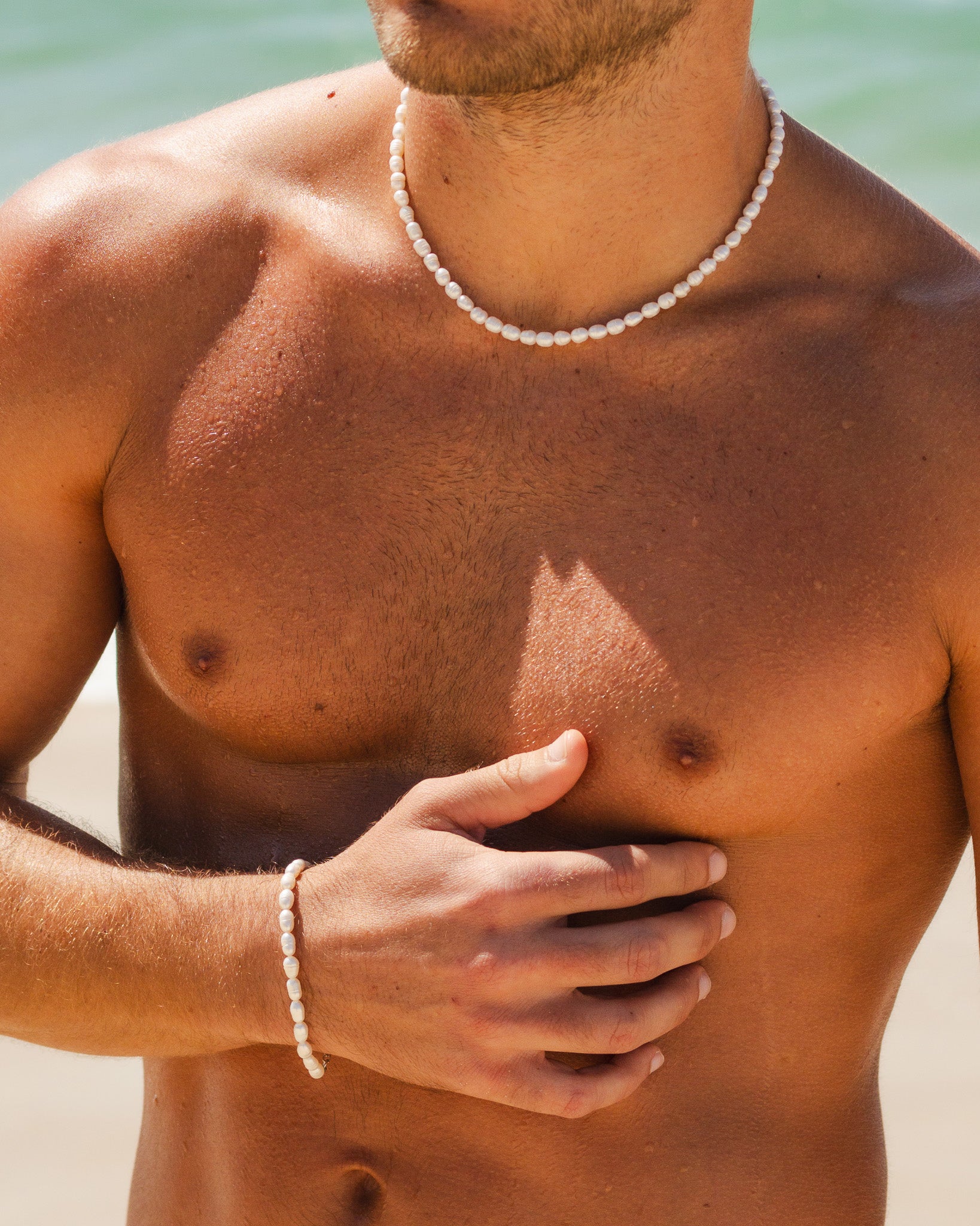 Close up of a white pearl bead necklace resting on a man's bare chest