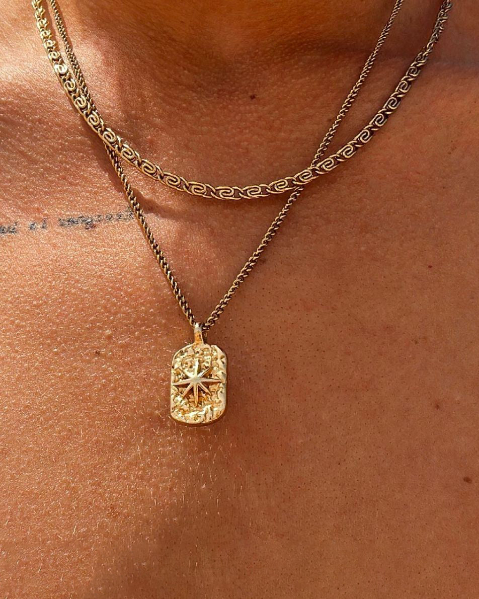 Gold layered necklaces on a man wearing a black shirt, with a carved rectangular pendant resting on the chest.