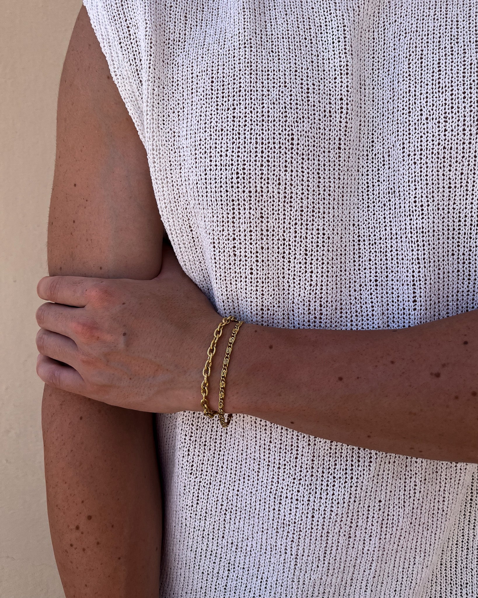 Gold chain bracelet worn on the wrist against a white knit fabric backdrop