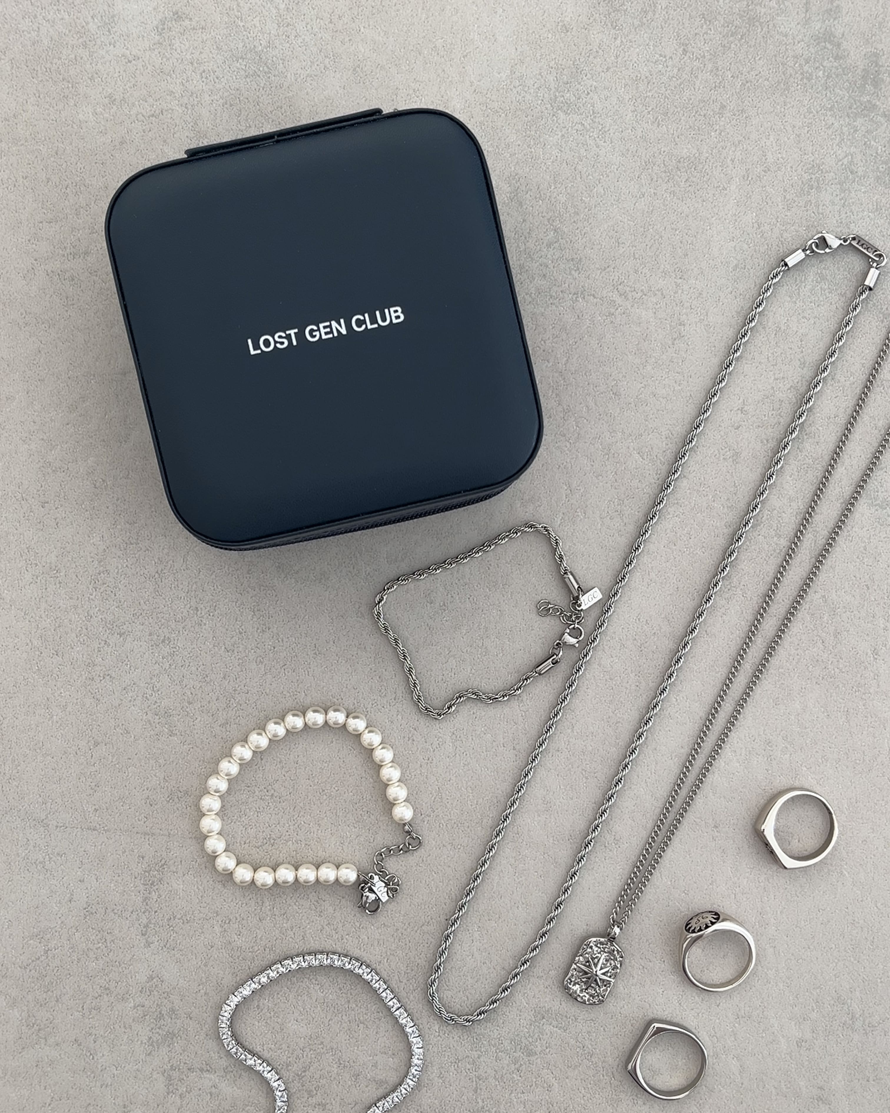 Dark blue travel jewelry case with Lost Gen Club logo beside silver chains