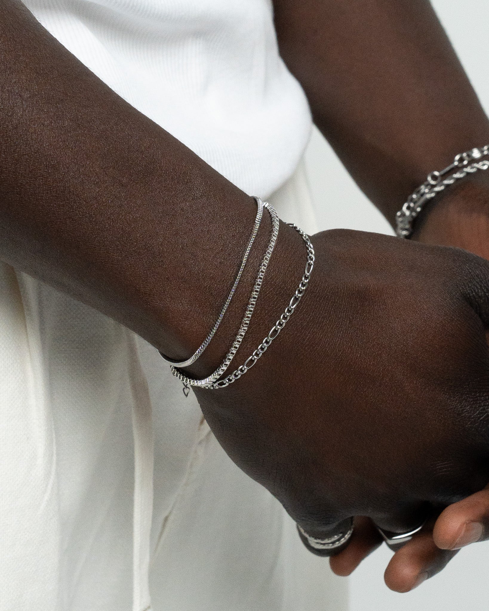 Side view of layered silver bracelets on a forearm with a white shirt in the background