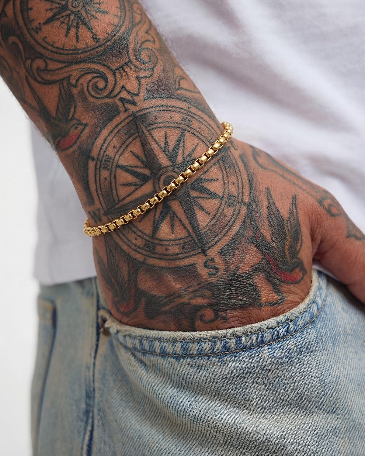 Noir Gold Bracelet worn on a tattooed wrist with a compass tattoo visible and denim in the background