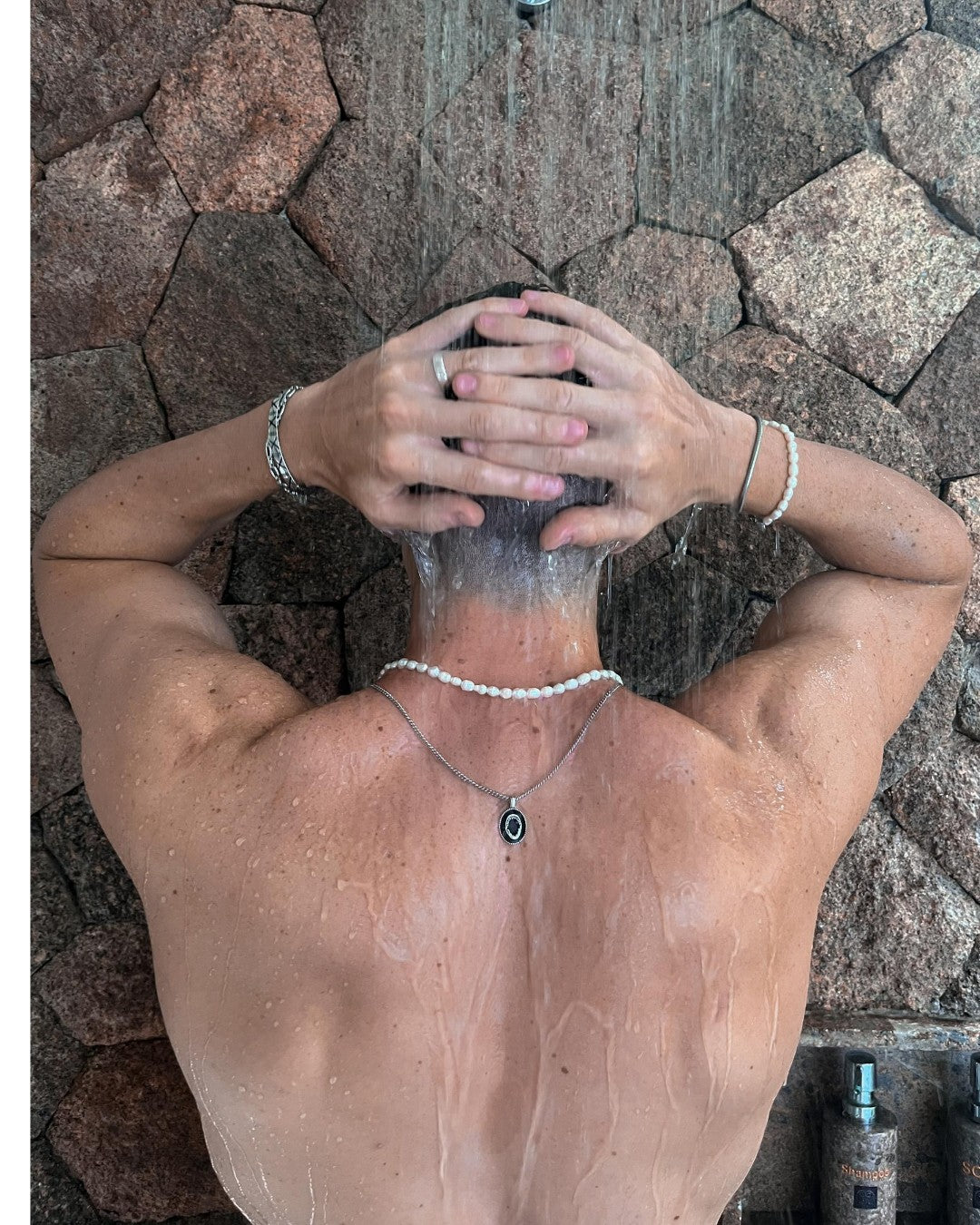 Back view of a shirtless person wearing a silver sharkjaw pendant necklace under a shower