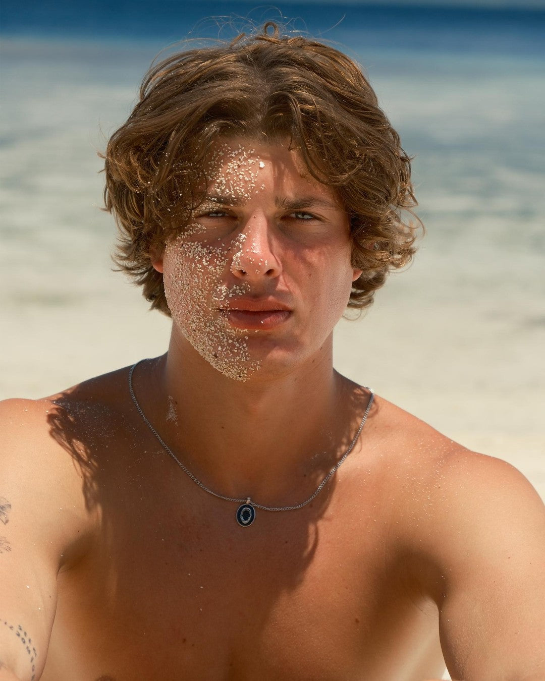 Young man on the beach wearing a silver sharkjaw pendant necklace with additional chains